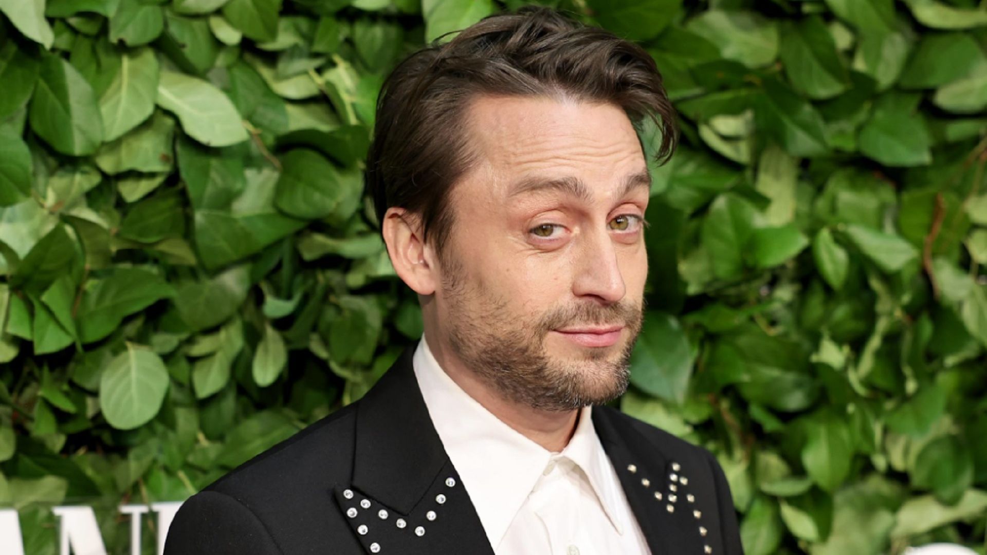 Kieran Culkin che guarda ironicamente la telecamera contro un muro di foglie