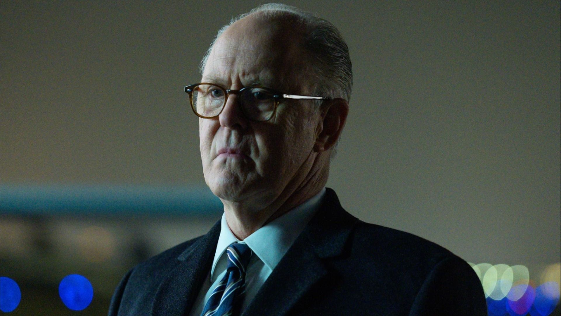 Attore John Lithgow in un abito e occhiali, sta immobile e guarda di lato