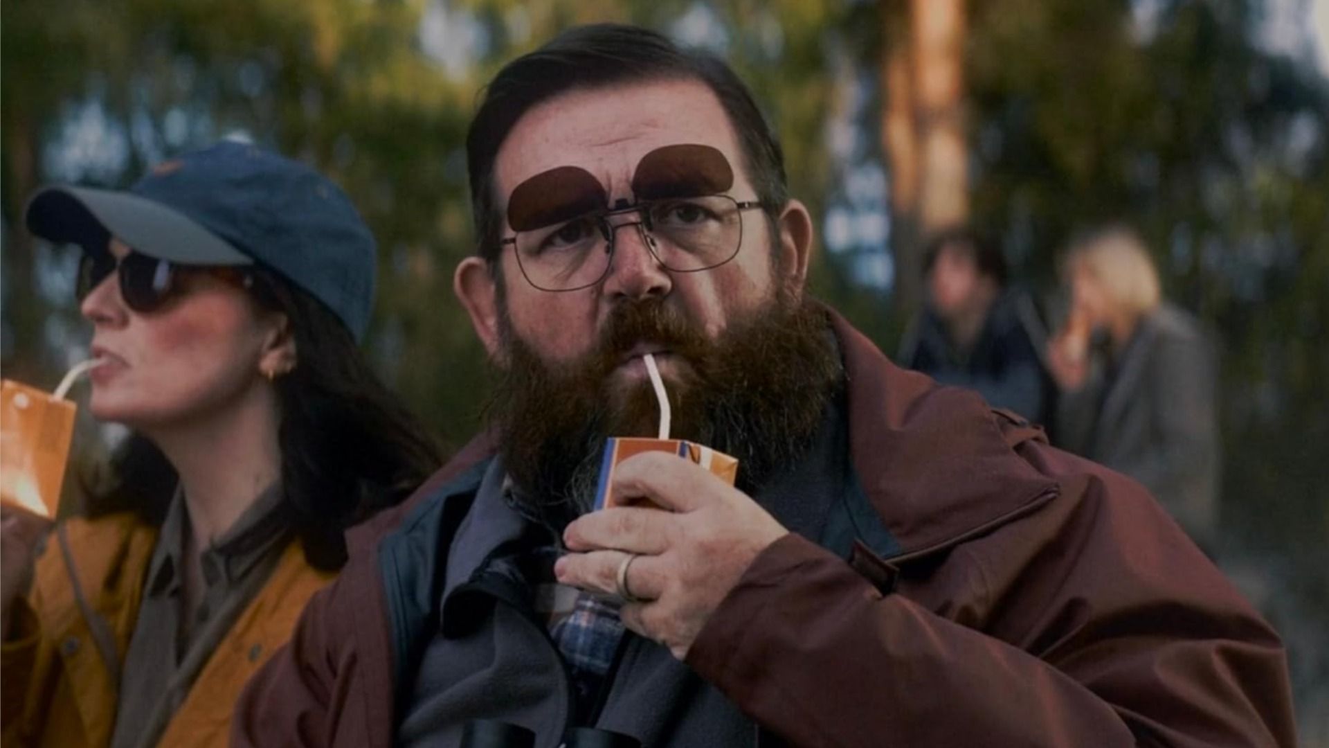 Attore Nick Frost in occhiali beve succo da una scatola di cartone con una cannuccia e guarda la fotocamera