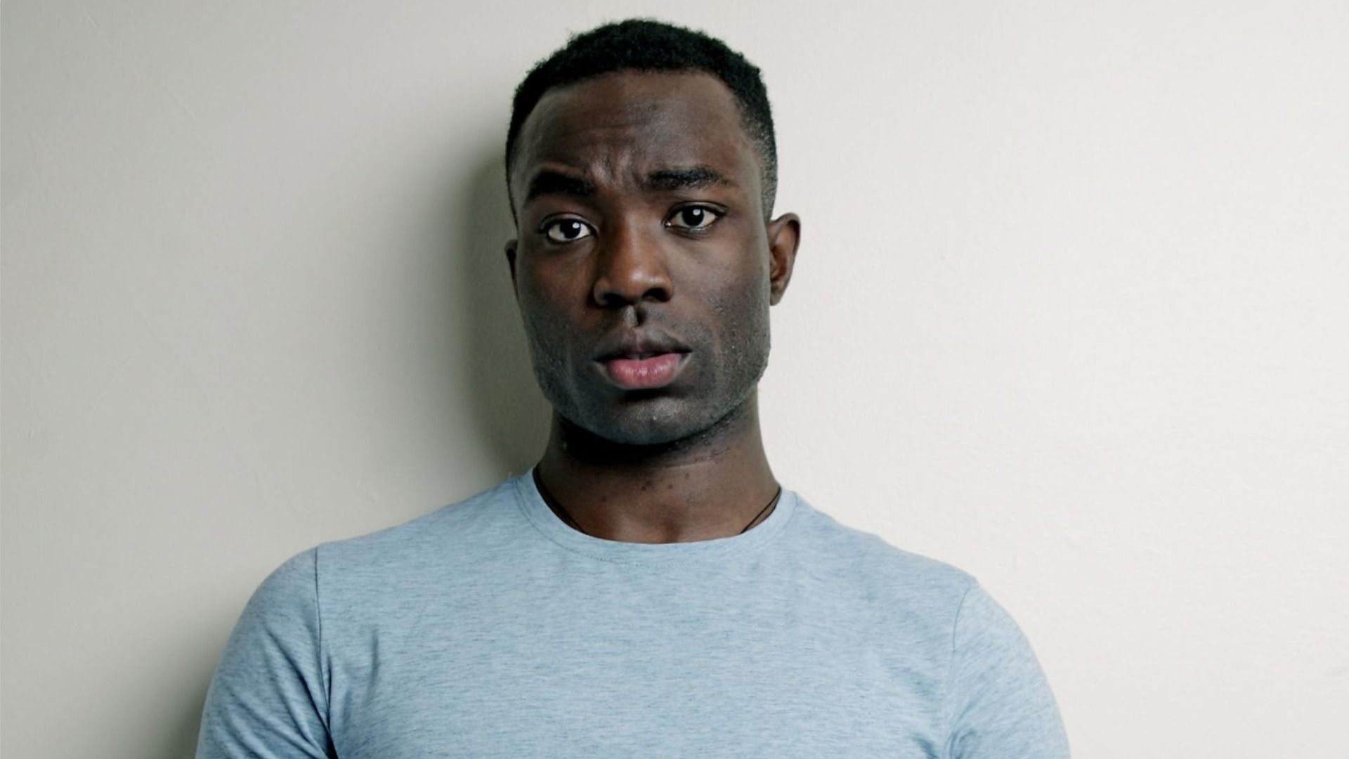 Attore Paapa Essiedu con abiti blu che guarda la fotocamera, sollevando un sopracciglio