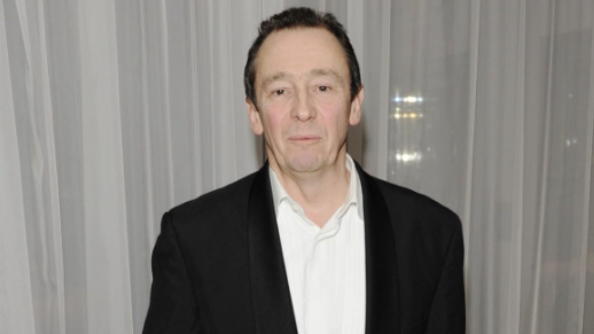 Attore Paul Whitehouse in un abito nero su uno sfondo di tulle bianco e guarda la fotocamera