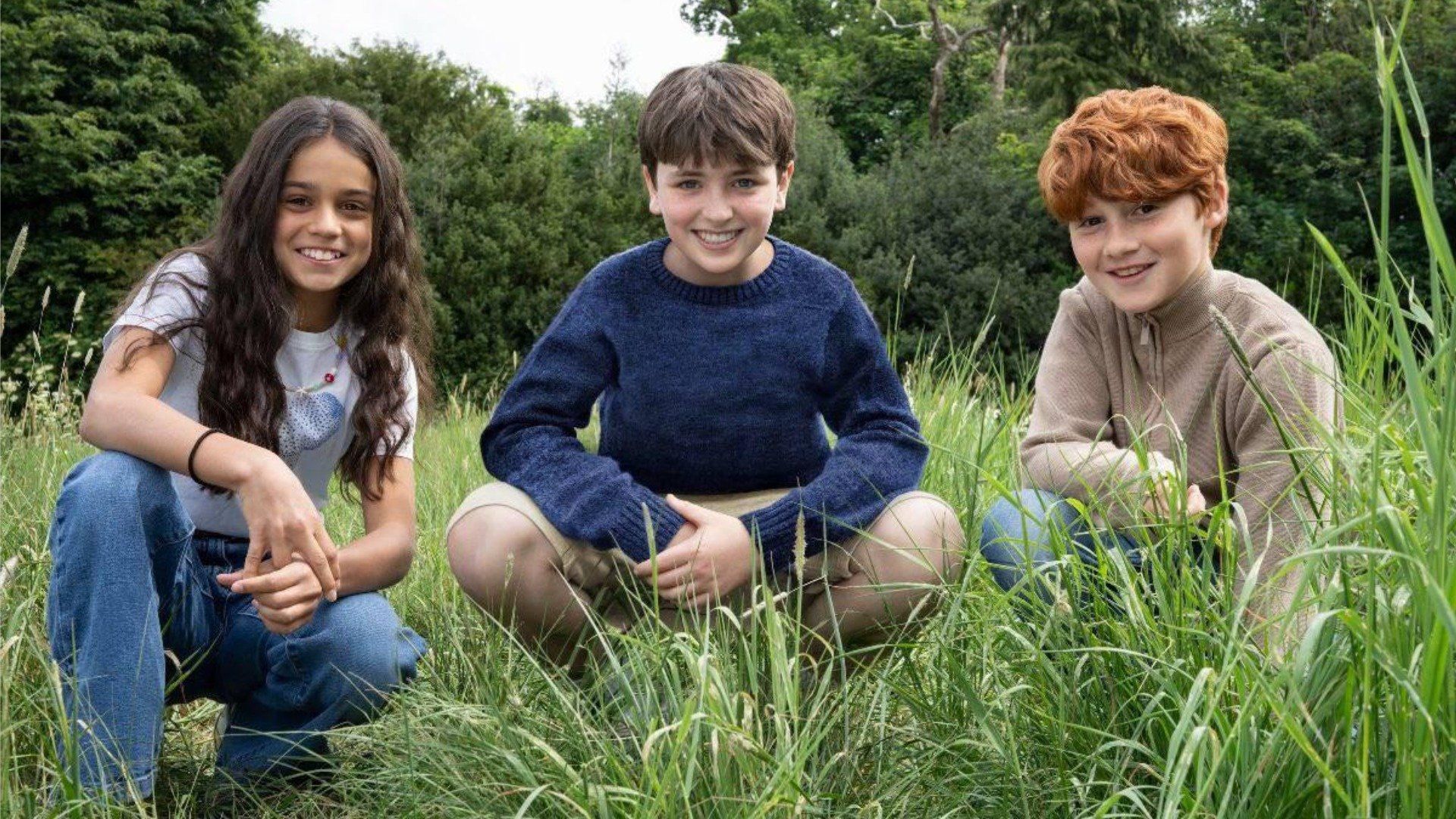 Attori Dominic McLaughlin, Alastair Stout e Arabella Stanton seduti sull'erba e sorridenti