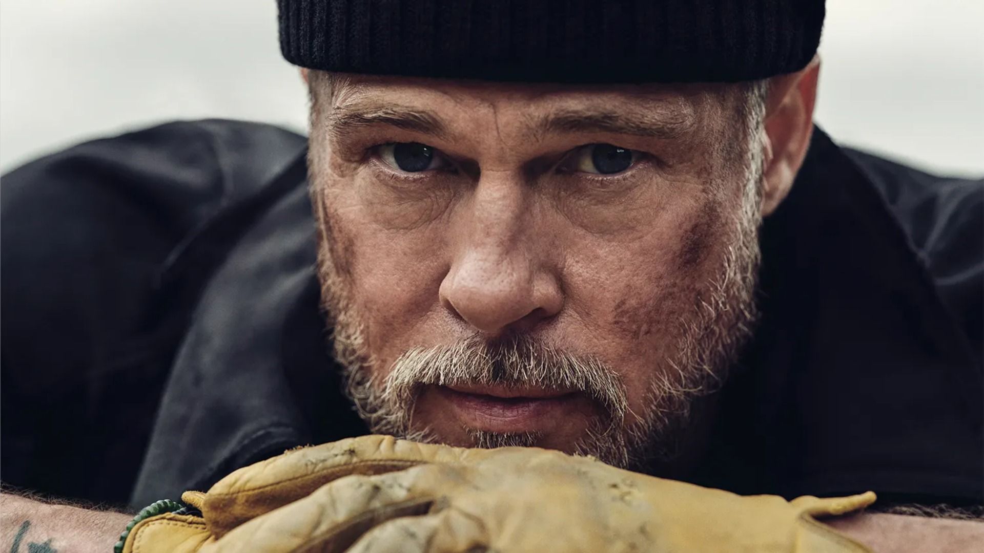 L'attore Brad Pitt con un cappello nero e guanti gialli che guarda la fotocamera