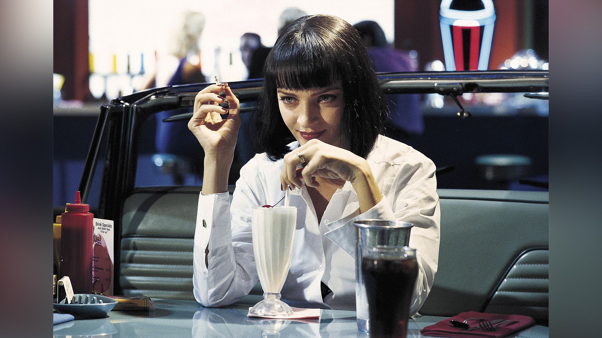 Uma Thurman in una camicia bianca beve un frappè in un caffè in una scena del film 'Pulp Fiction'