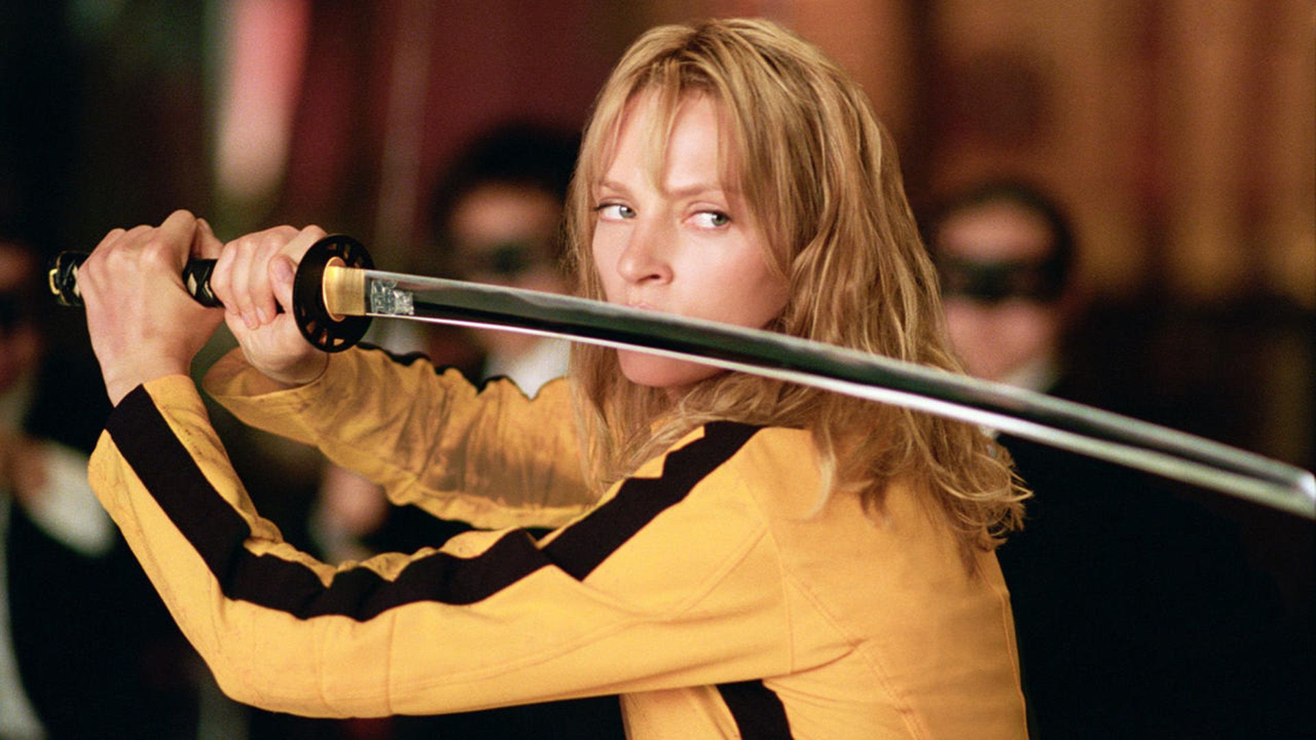 Uma Thurman in a yellow sweater with black stripes holds a katana in front of her face in 'Kill Bill'