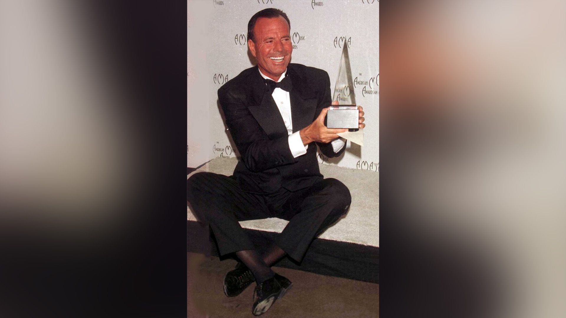 Un felice Julio Iglesias in un abito nero tiene in mano il trofeo degli American Music Awards