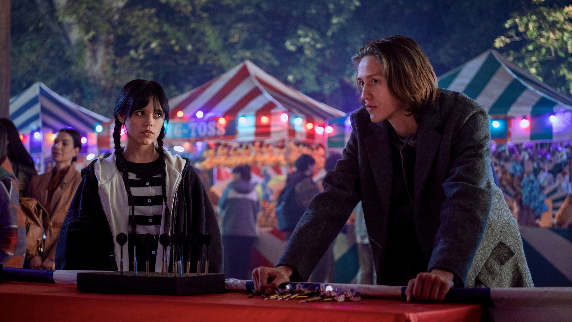 Jenna Ortega e Percy Hynes White in primo piano con una fiera sullo sfondo