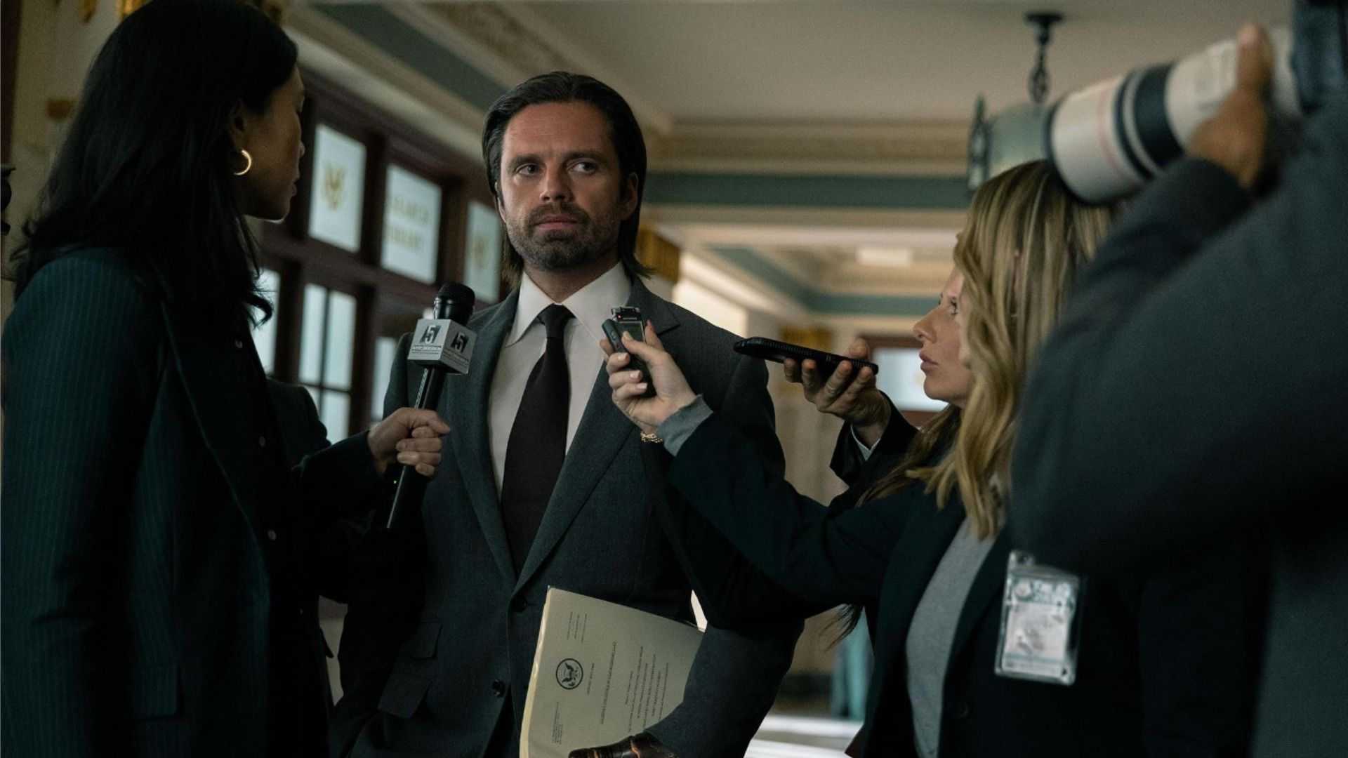 L'attore Sebastian Stan in un abito nero con i capelli lunghi circondato da giornalisti
