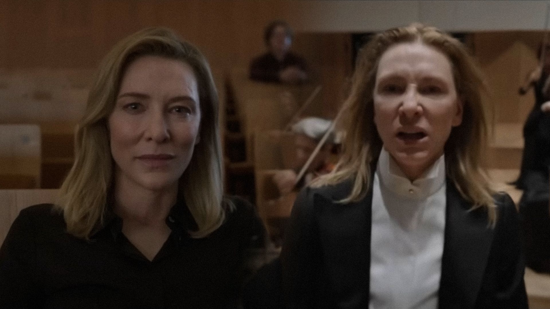 L'attrice Cate Blanchett in un abito nero fissa minacciosamente la telecamera su uno sfondo di violinisti