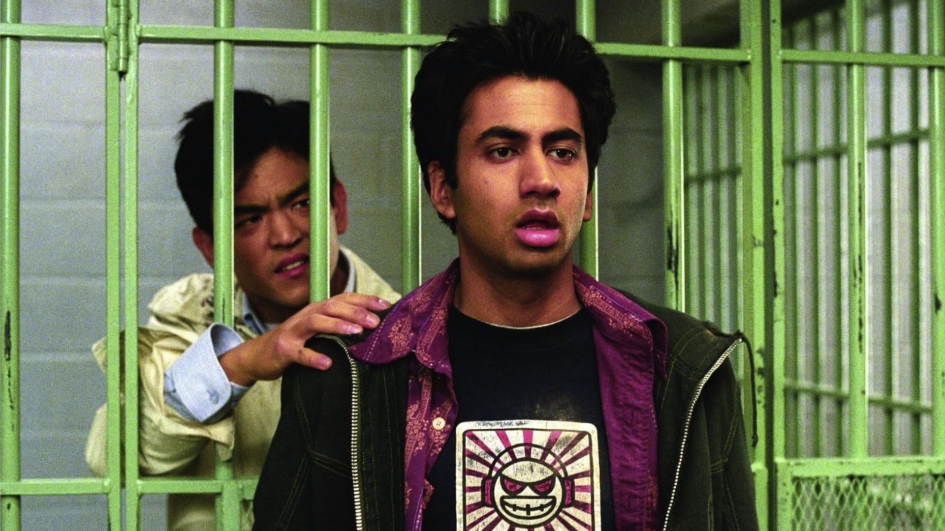 L'attore John Cho sta dietro le sbarre verdi della prigione, l'attore Kal Penn sta fuori e guarda di lato