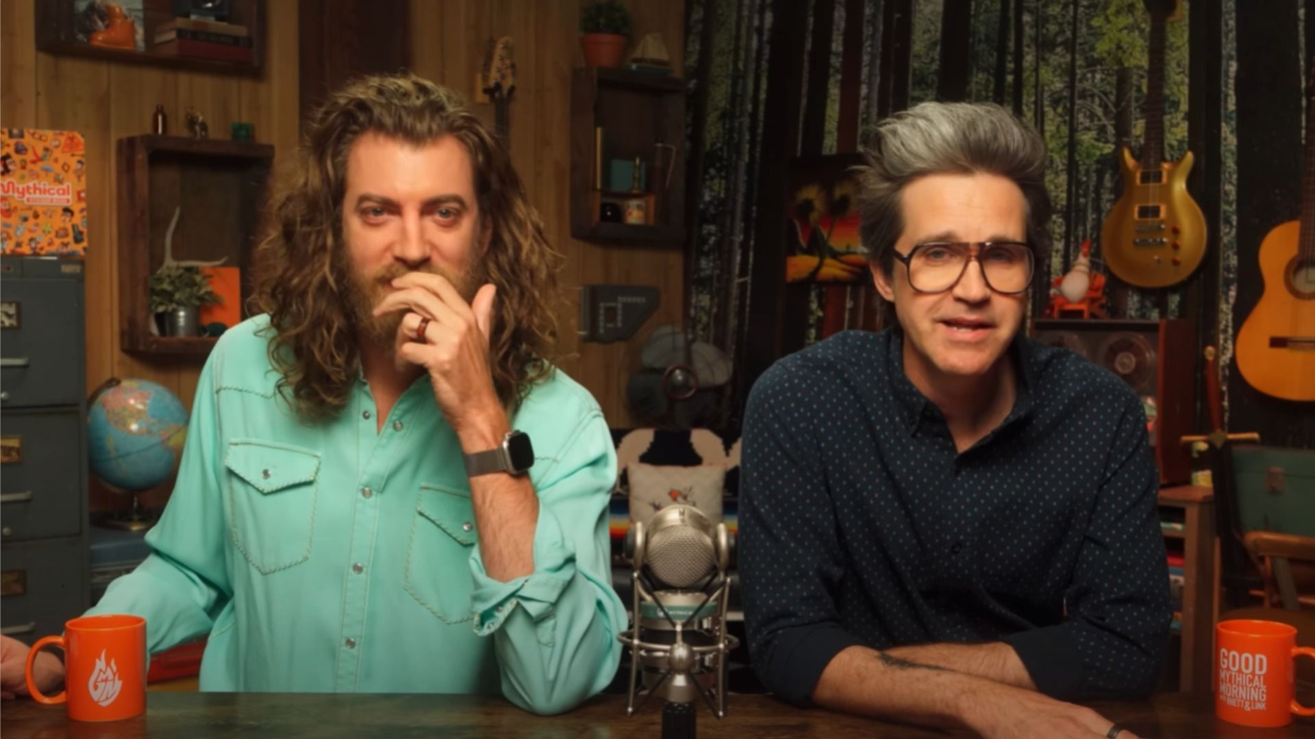 I blogger Rhett e Link in camicia seduti a un tavolo vicino al microfono