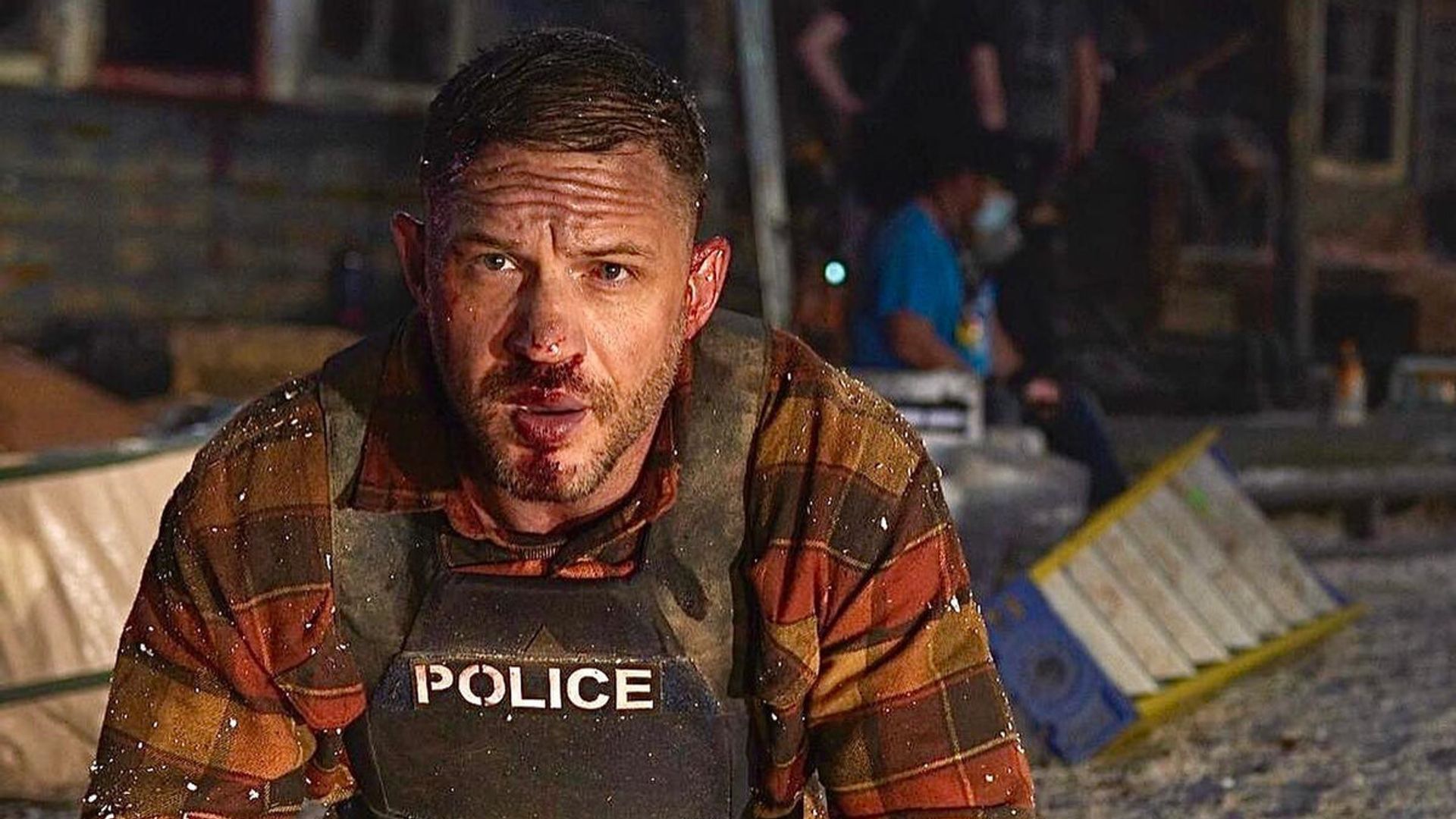 Tom Hardy in giubbotto antiproiettile con il volto contuso è inginocchiato sulla scena dell'incidente