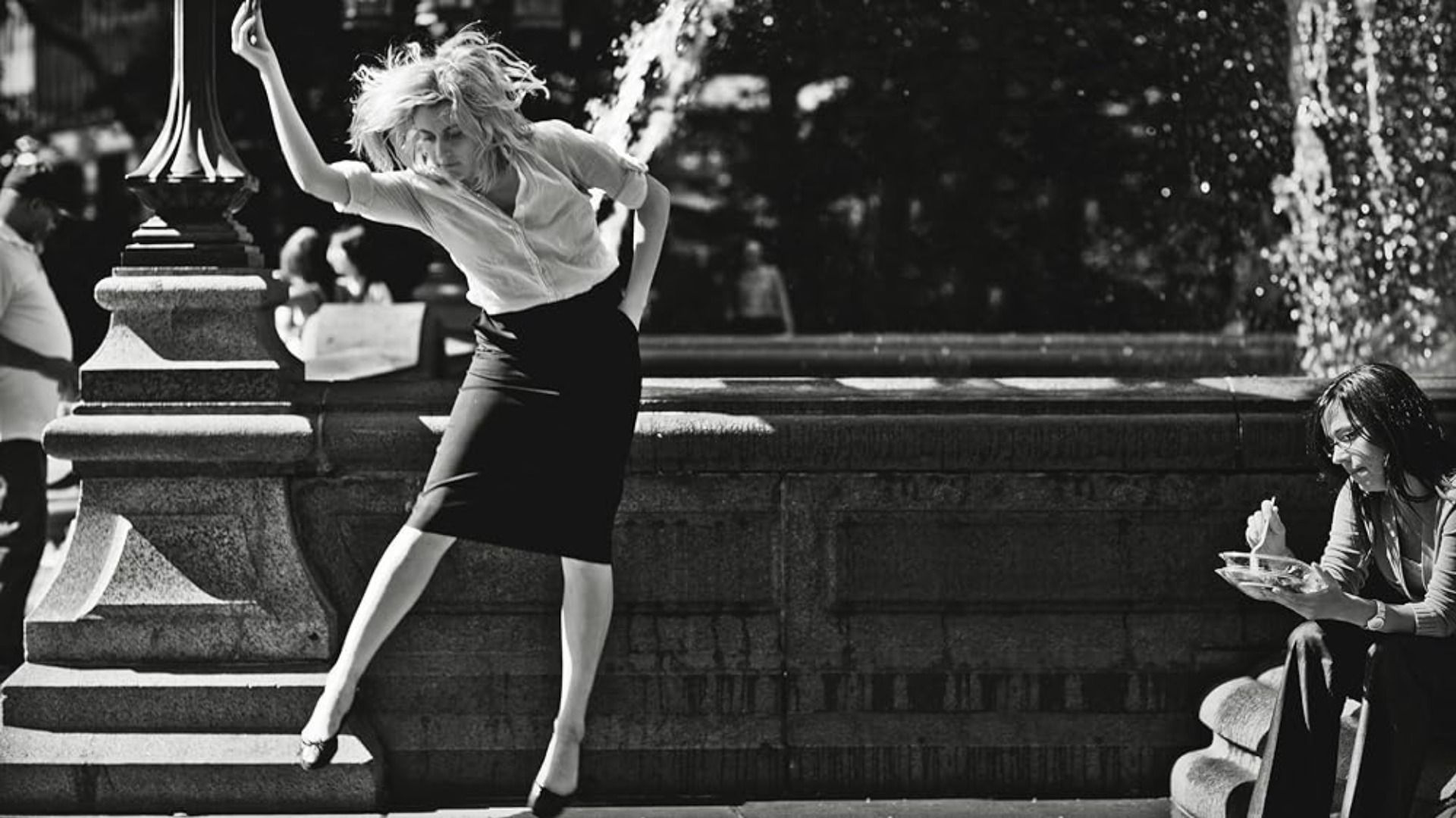 L'attrice Greta Gerwig danza con una camicetta bianca e gonna nera sullo sfondo di una fontana