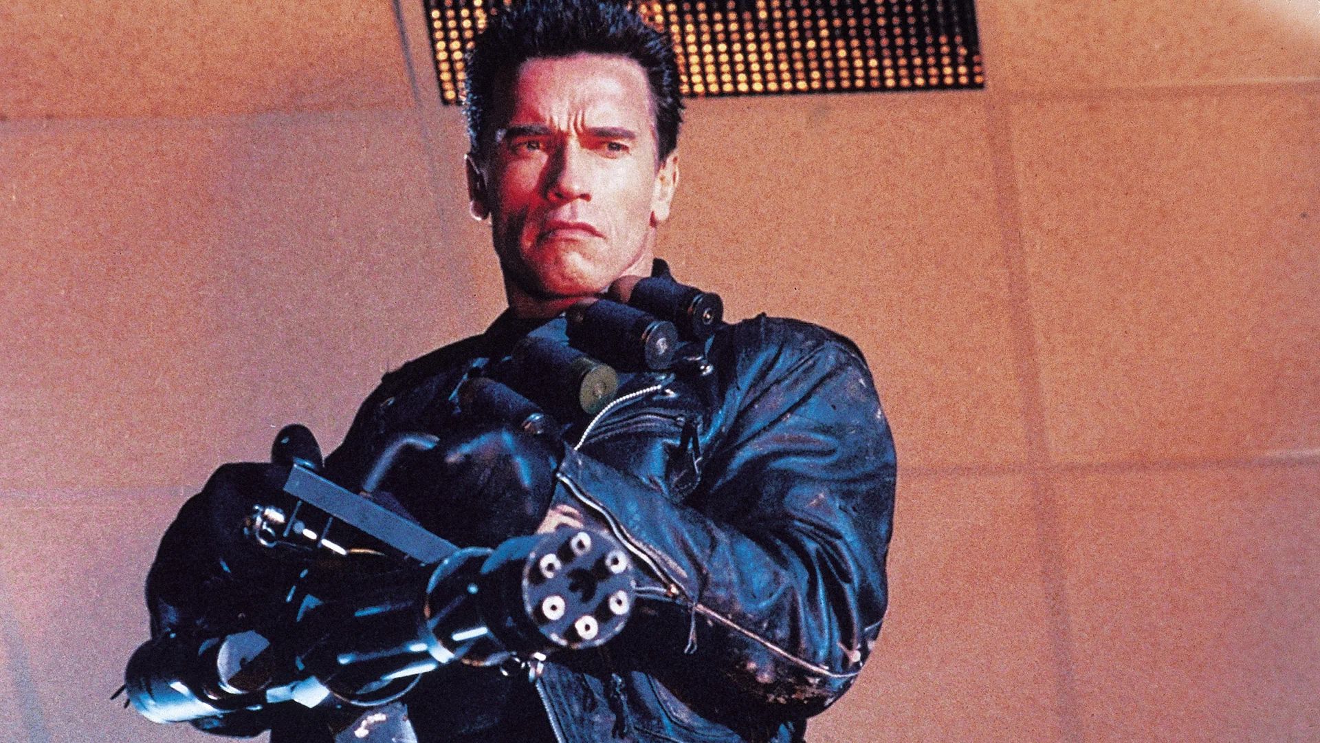 Arnold Schwarzenegger in giacca di pelle nera che impugna una minigun