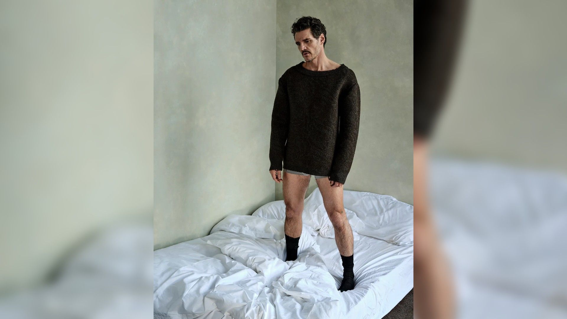 Pedro Pascal in piedi su un letto con un maglione e biancheria intima
