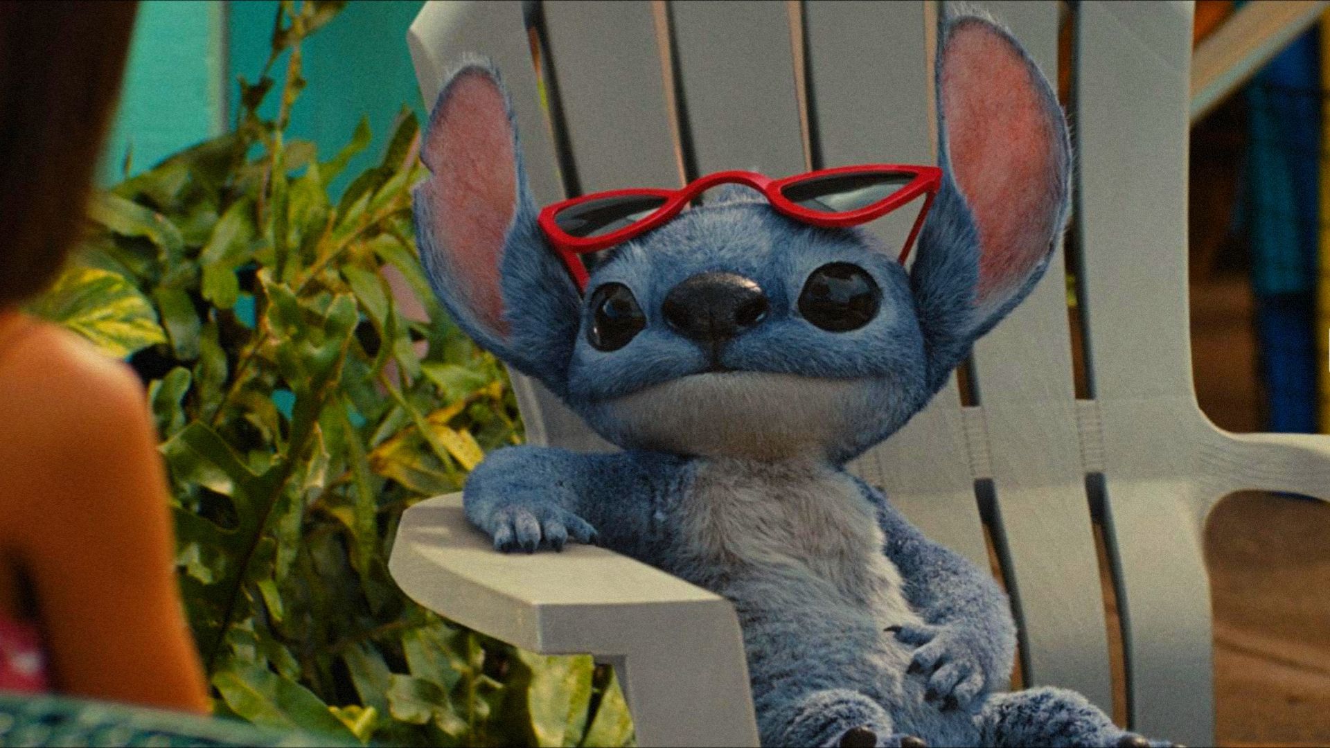 L'alieno blu Stitch seduto su una sedia a sdraio con gli occhiali che guarda di lato