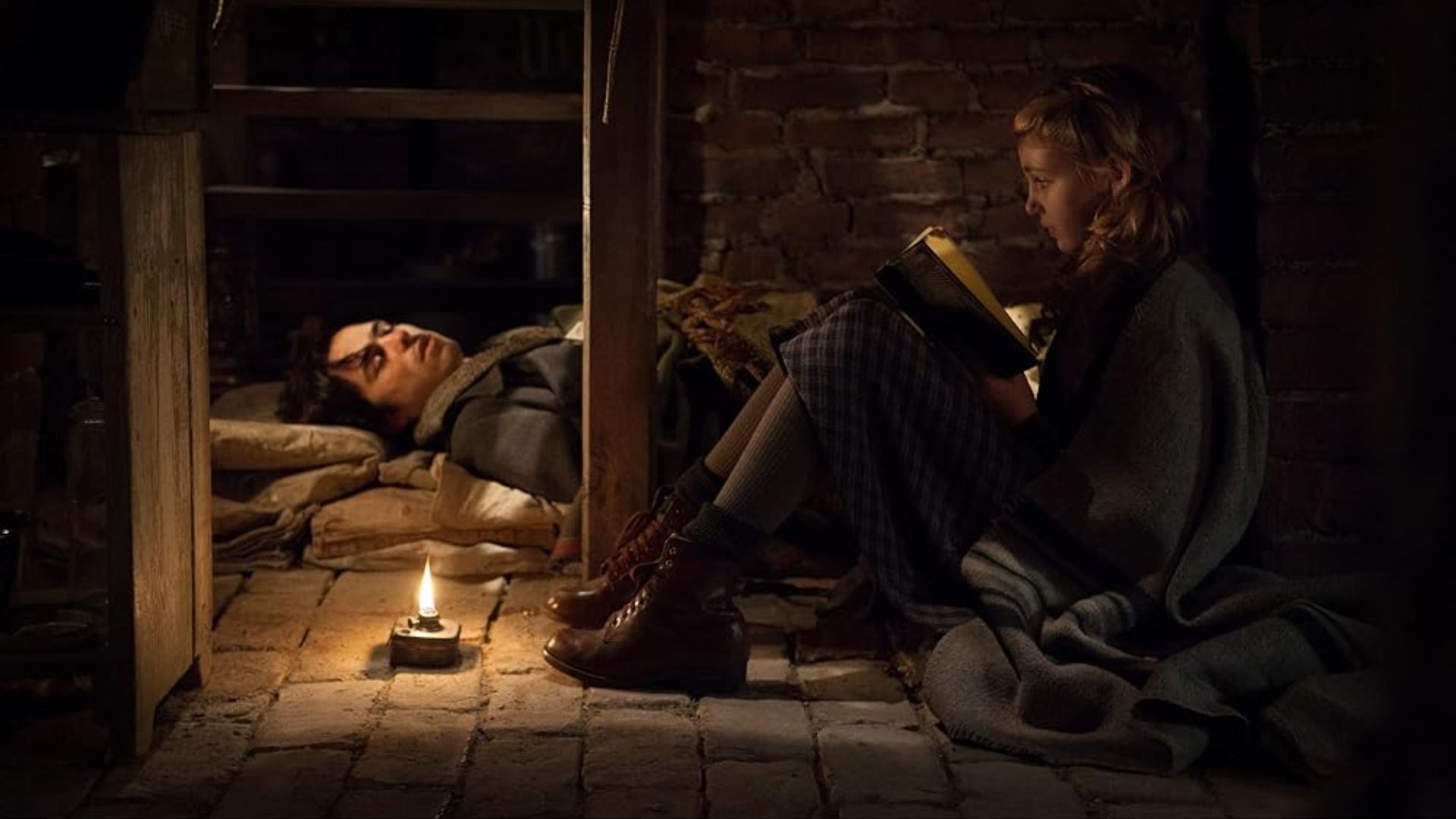 L'attrice Sophie Nélisse seduta in un seminterrato con un libro tra le mani vicino a un uomo che dorme sul pavimento