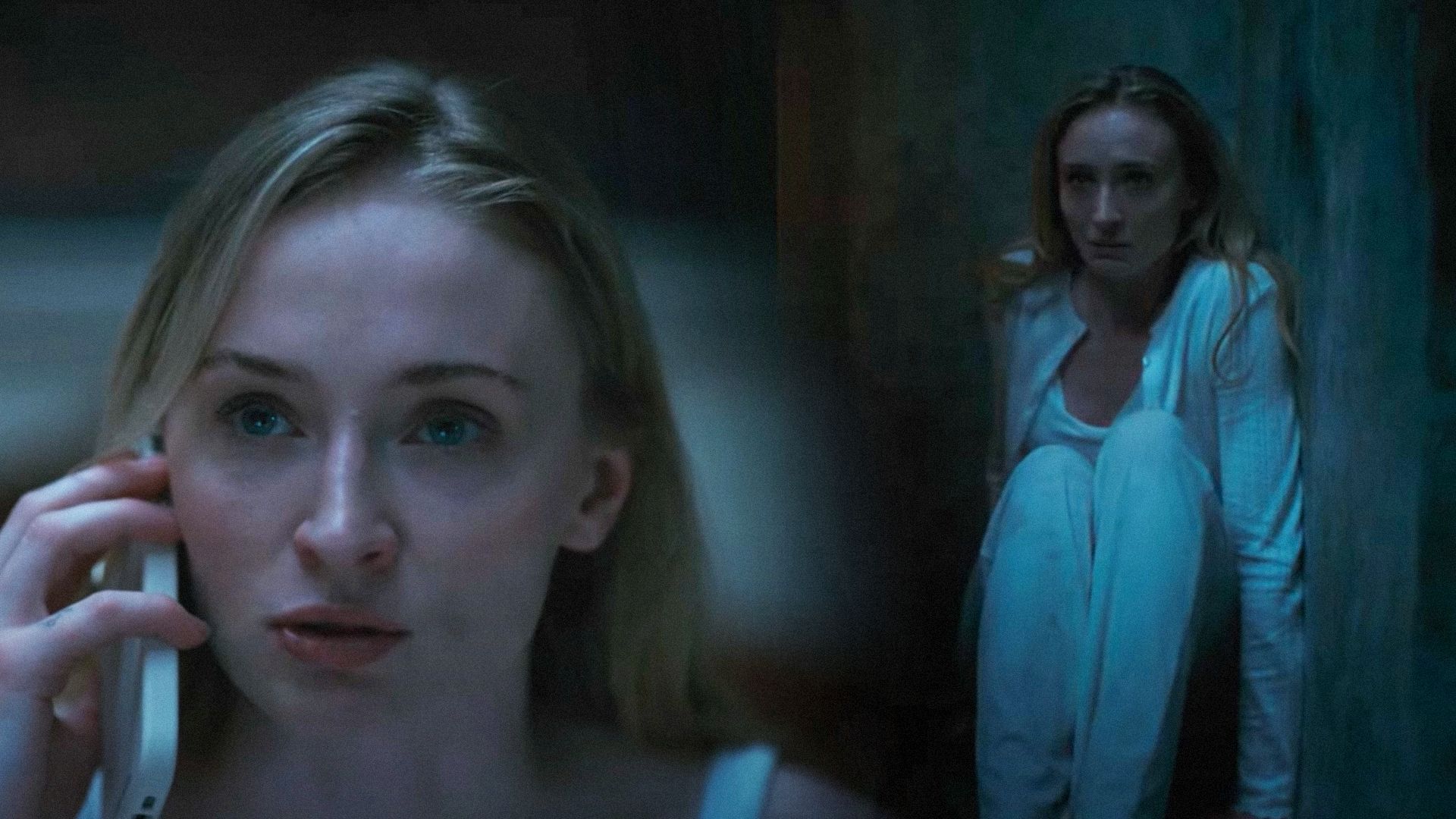 L'attrice Sophie Turner con un telefono in mano seduta contro il muro in camicia da notte