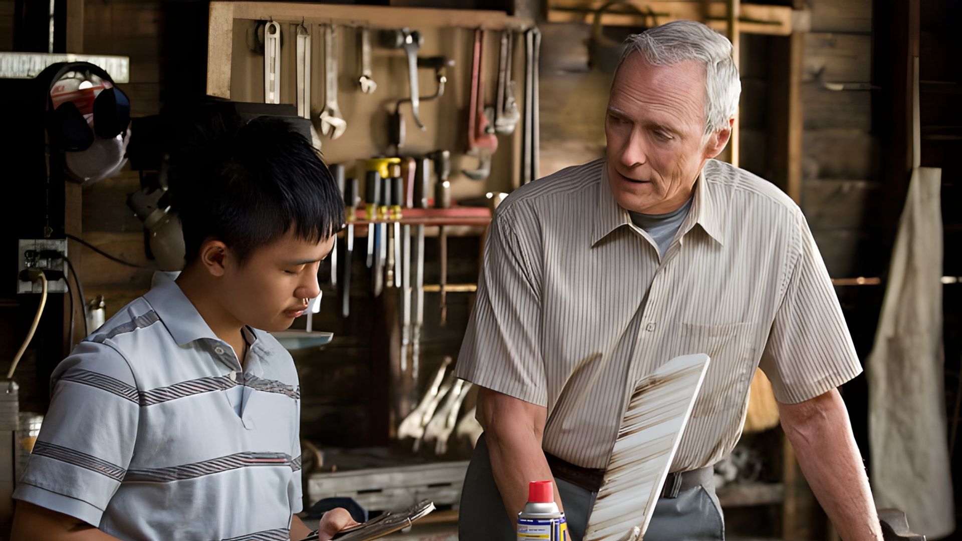 Clint Eastwood e un ragazzo lavorano in un'officina, discutendo di un attrezzo sullo sfondo di un banco da lavoro con utensili appesi