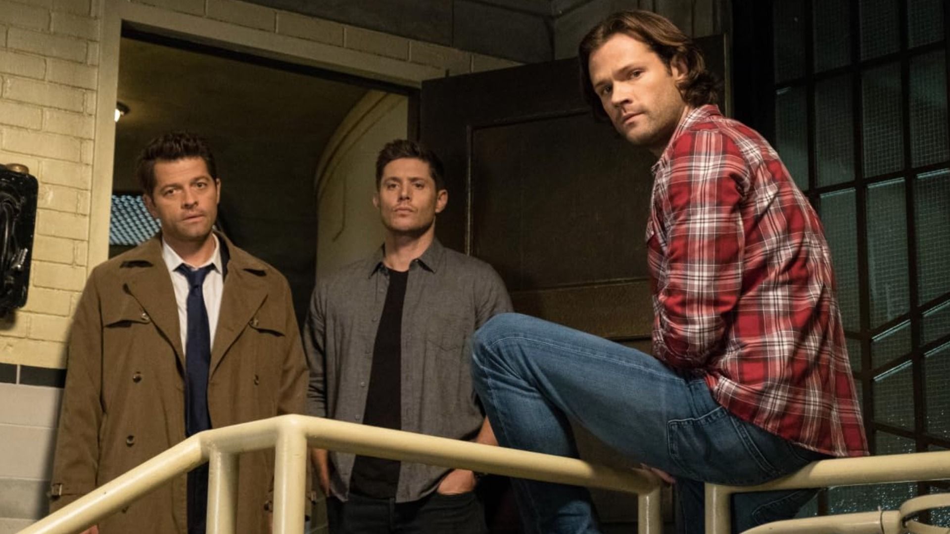 Gli attori Misha Collins, Jensen Ackles e Jared Padalecki stanno in piedi vicino alla porta guardando in basso