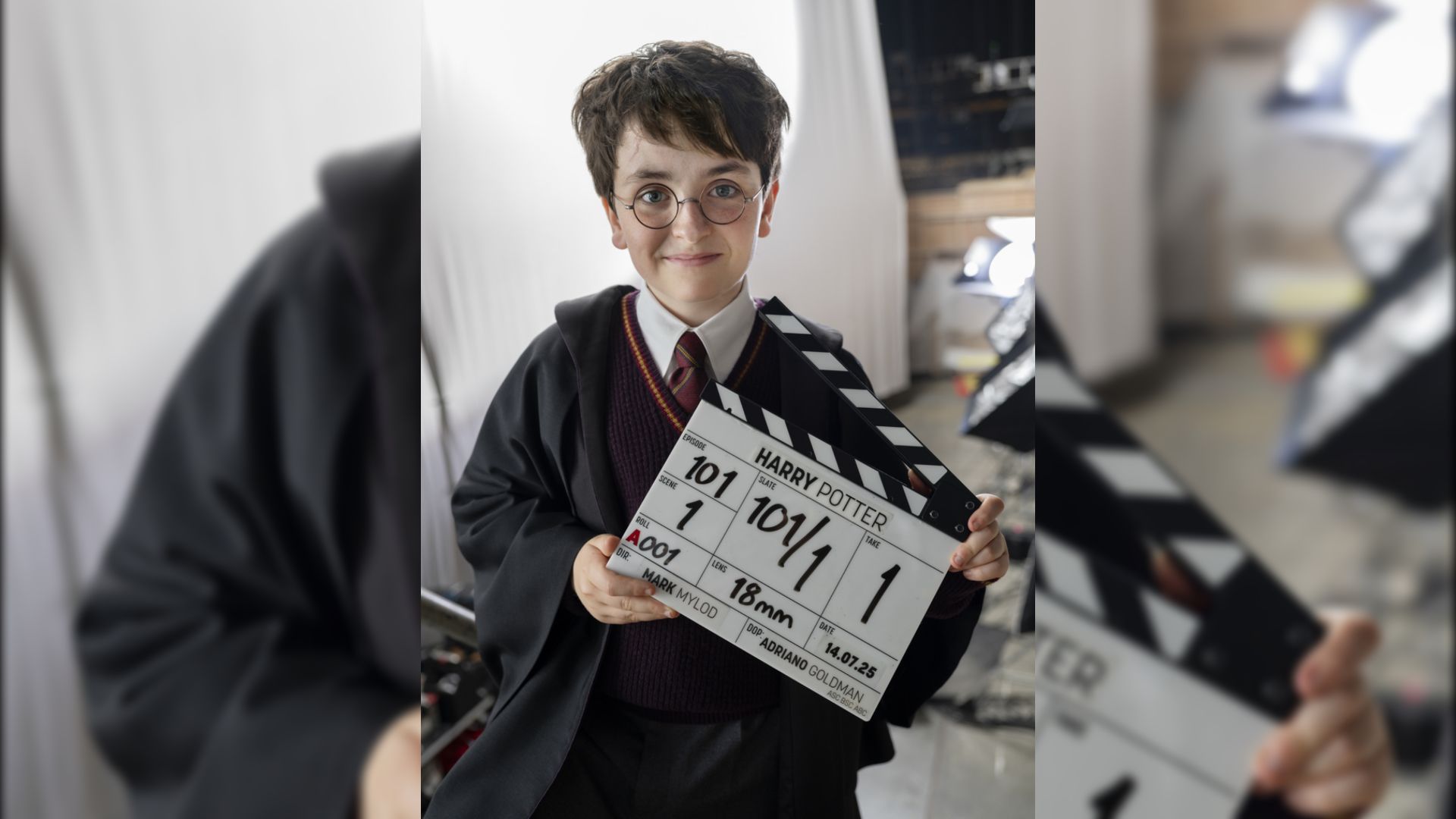 L'attore Dominic McLaughlin in mantello nero e occhiali tiene un ciak