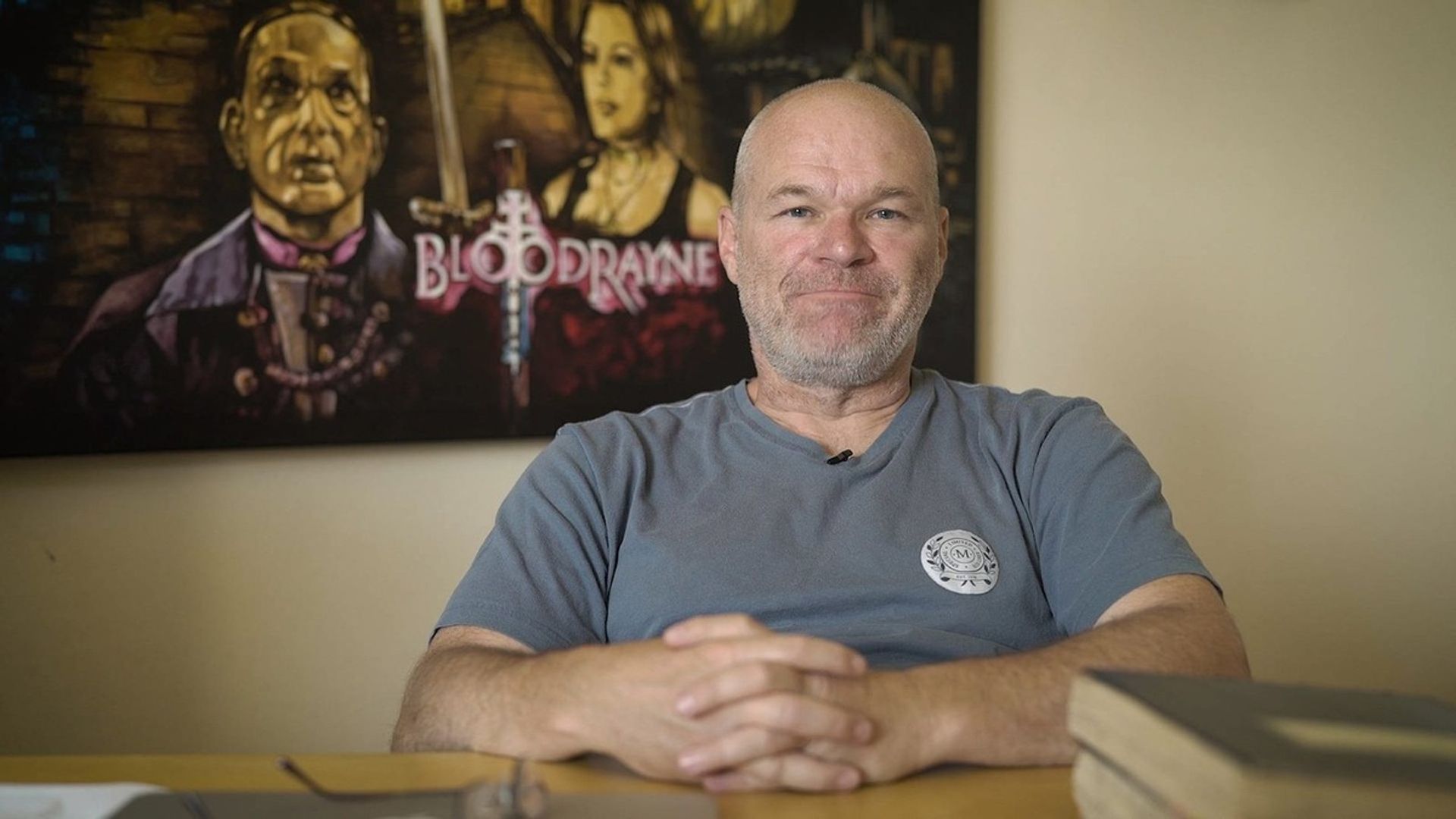 Il regista Uwe Boll sullo sfondo del poster del film BloodRayne