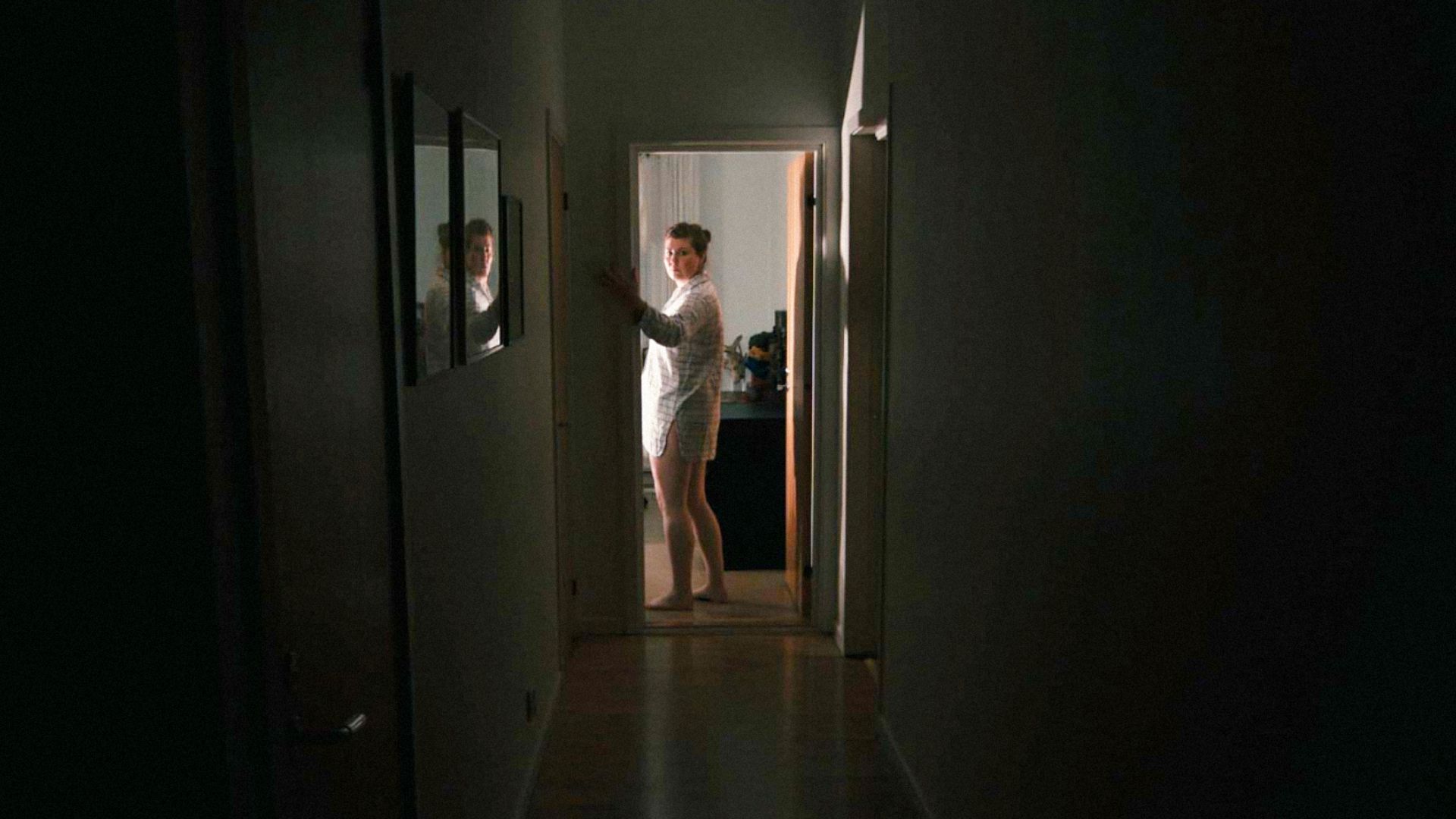 Una donna in camicia da notte sta in mezzo al corridoio azionando l'interruttore della luce