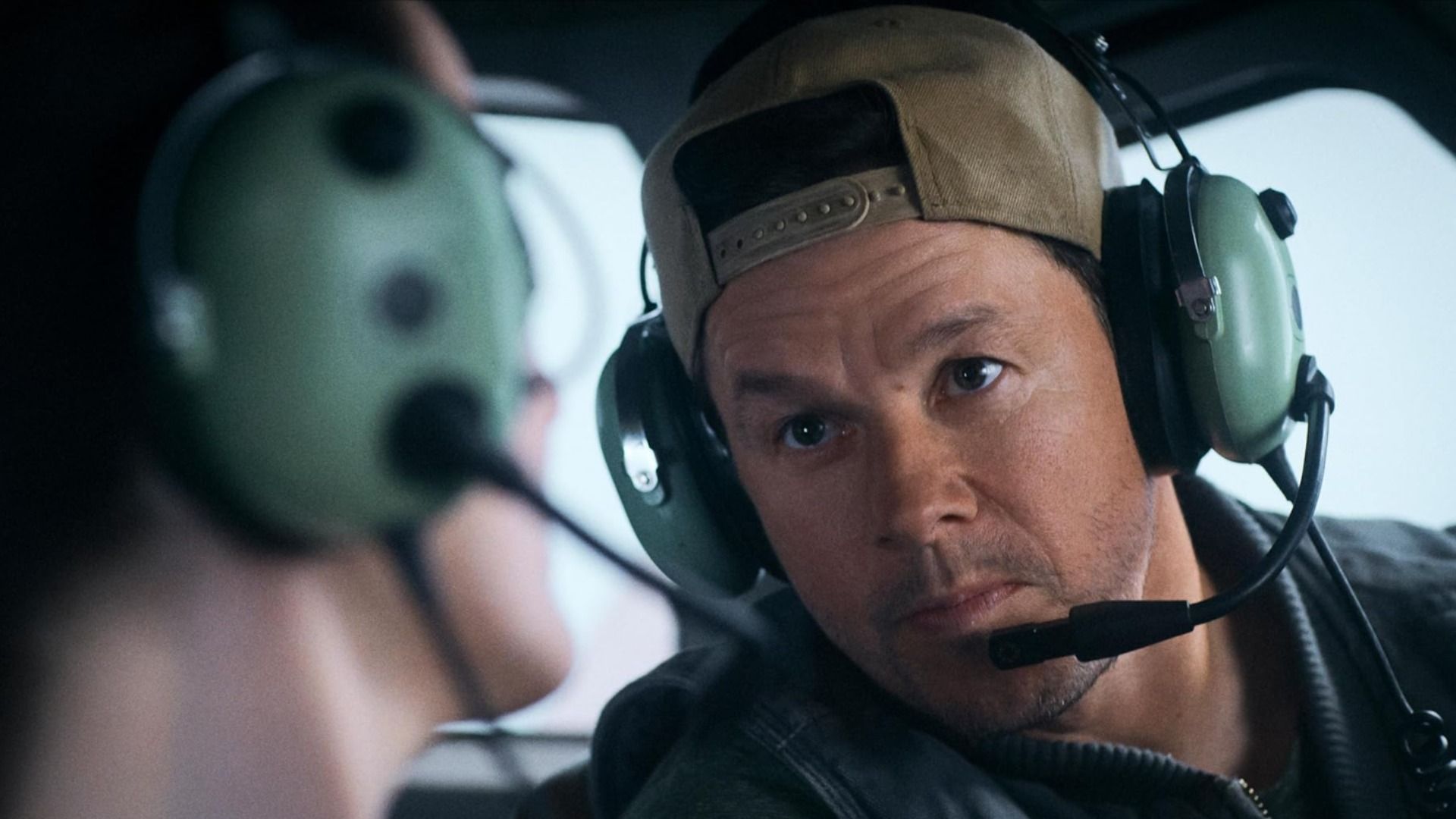 L'attore Mark Wahlberg con cappello e cuffie con microfono seduto su un aereo