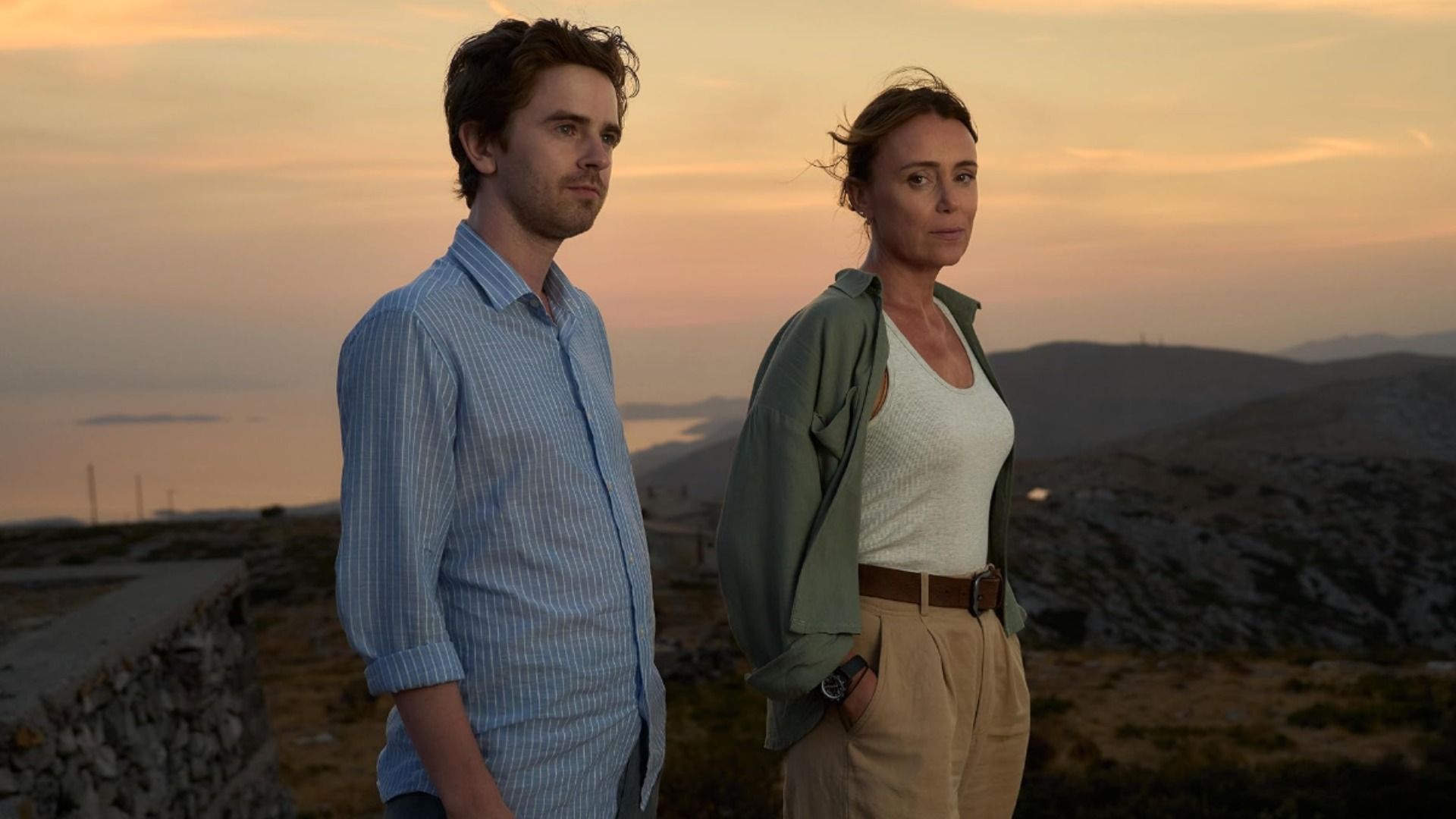 L'attore Freddie Highmore in camicia blu e l'attrice Keeley Hawes in canottiera bianca sullo sfondo di montagne