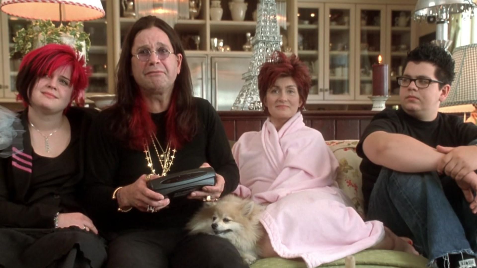 Il cantante Ozzy Osbourne in completo nero con catene seduto su un divano con moglie e figli