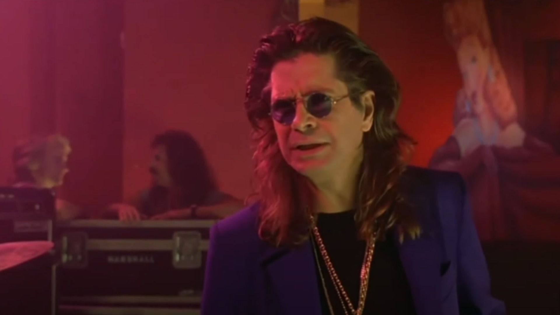 Il cantante Ozzy Osbourne in blazer blu e catena d'oro in piedi sul palco