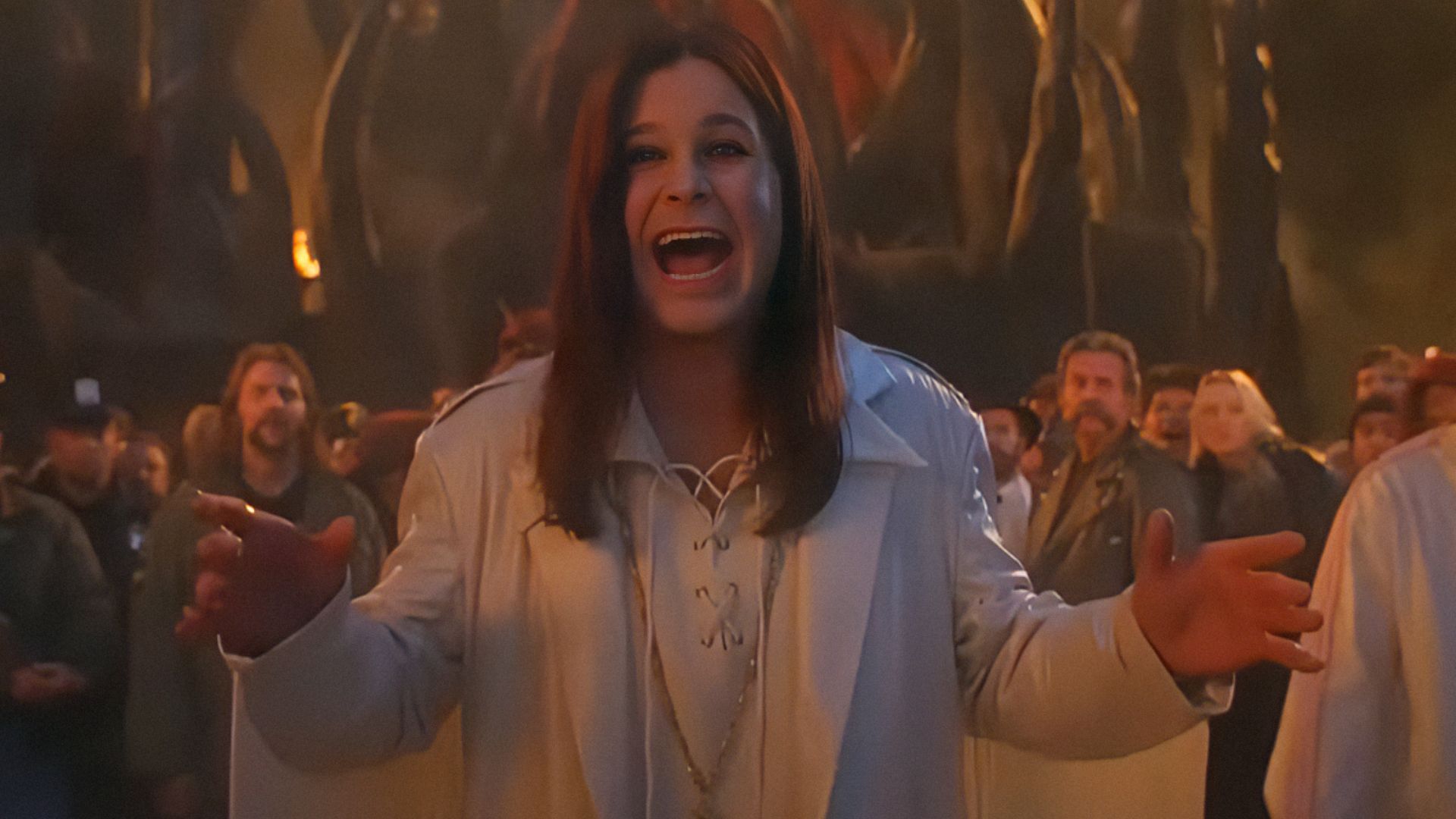 Il cantante Ozzy Osbourne in giacca bianca allarga le braccia e sorride