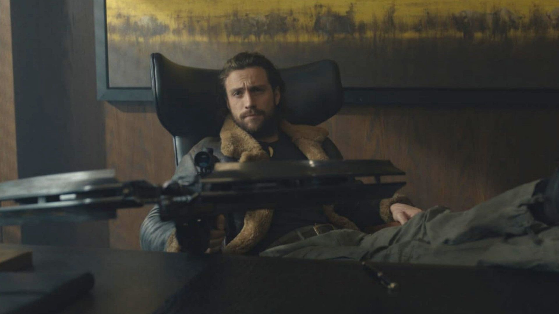 L'attore Aaron Taylor-Johnson seduto a un tavolo con una balestra tra le mani