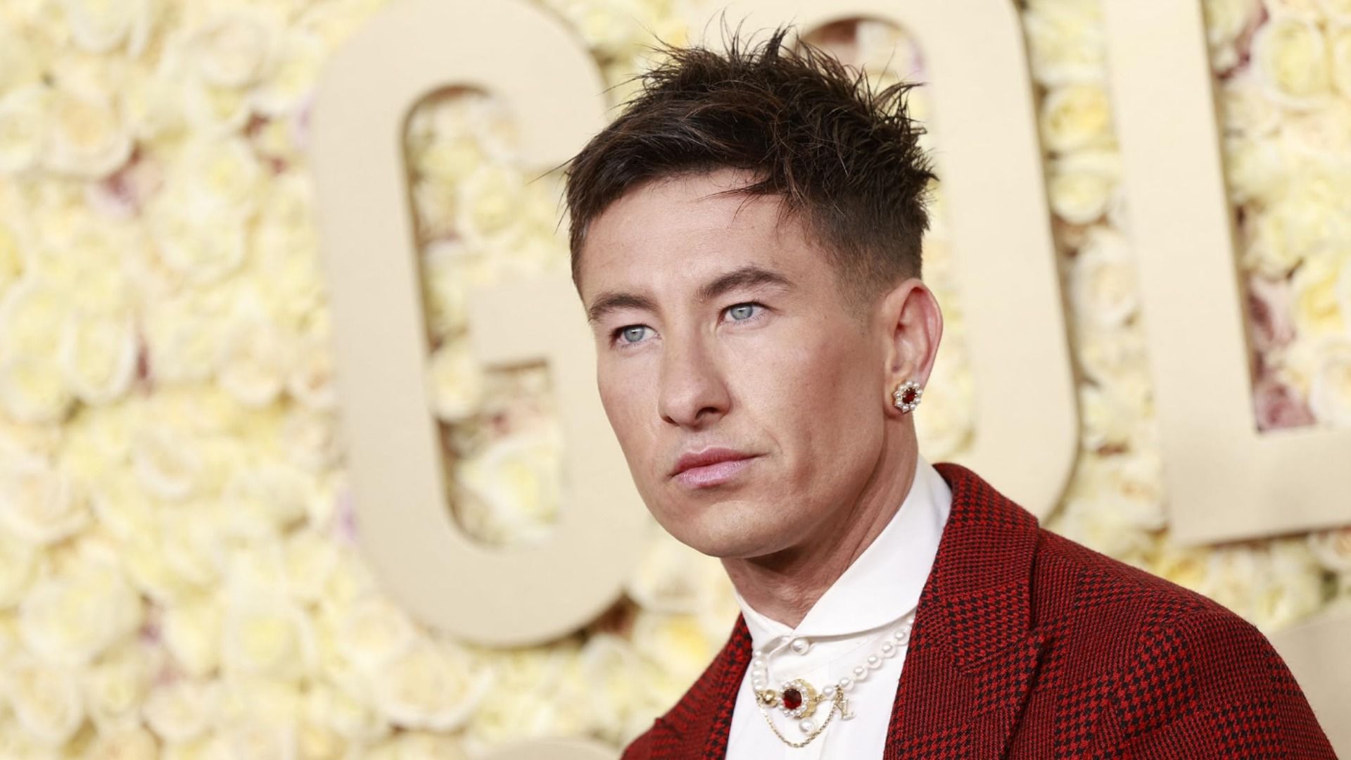 L'attore Barry Keoghan in giacca rossa con orecchino su sfondo giallo