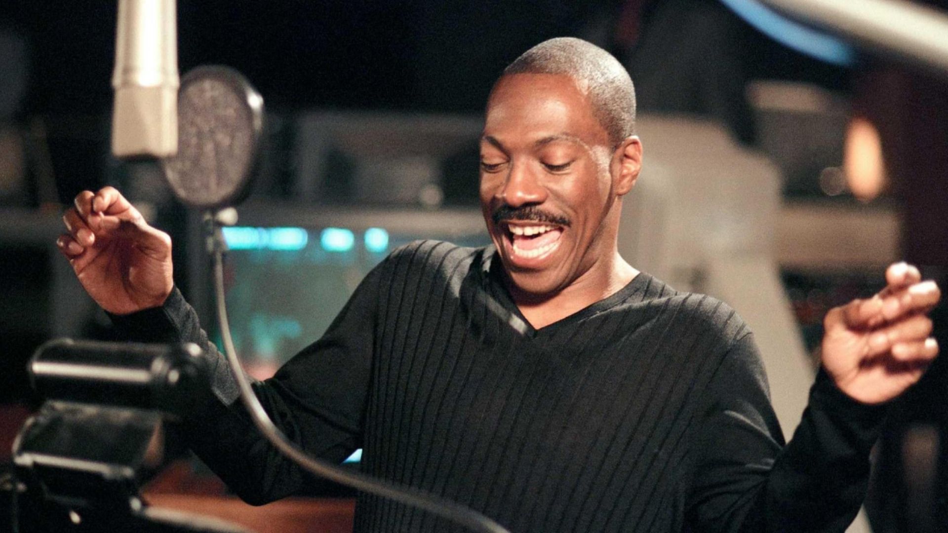 L'attore Eddie Murphy in un maglione nero sta davanti a un microfono e sorride