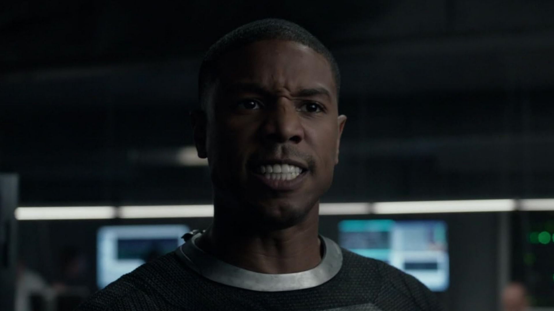 L'attore Michael B. Jordan in completo grigio con espressione arrabbiata su sfondo sfocato