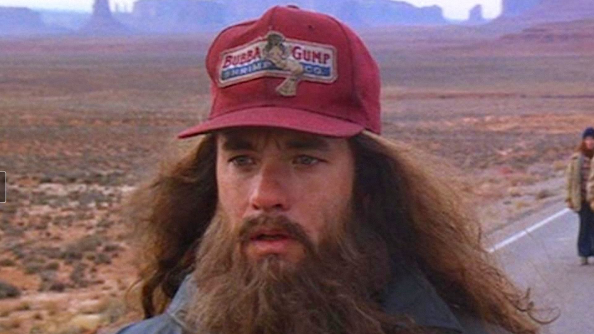 L'attore Tom Hanks con capelli lunghi e barba in piedi indossando un berretto rosso