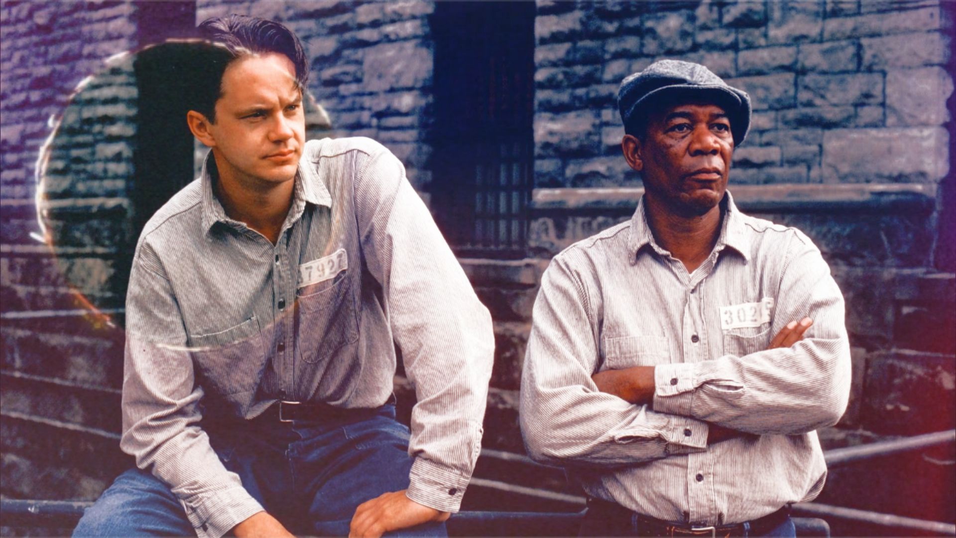 Gli attori Tim Robbins e Morgan Freeman in uniforme carceraria seduti accanto a un muro di pietra