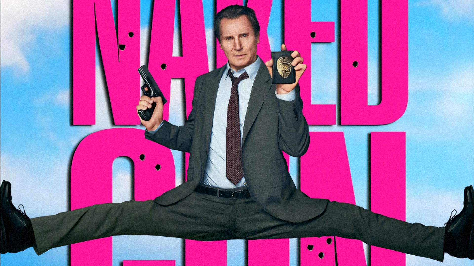 L'attore Liam Neeson seduto in spaccata con una pistola in mano e un distintivo da poliziotto