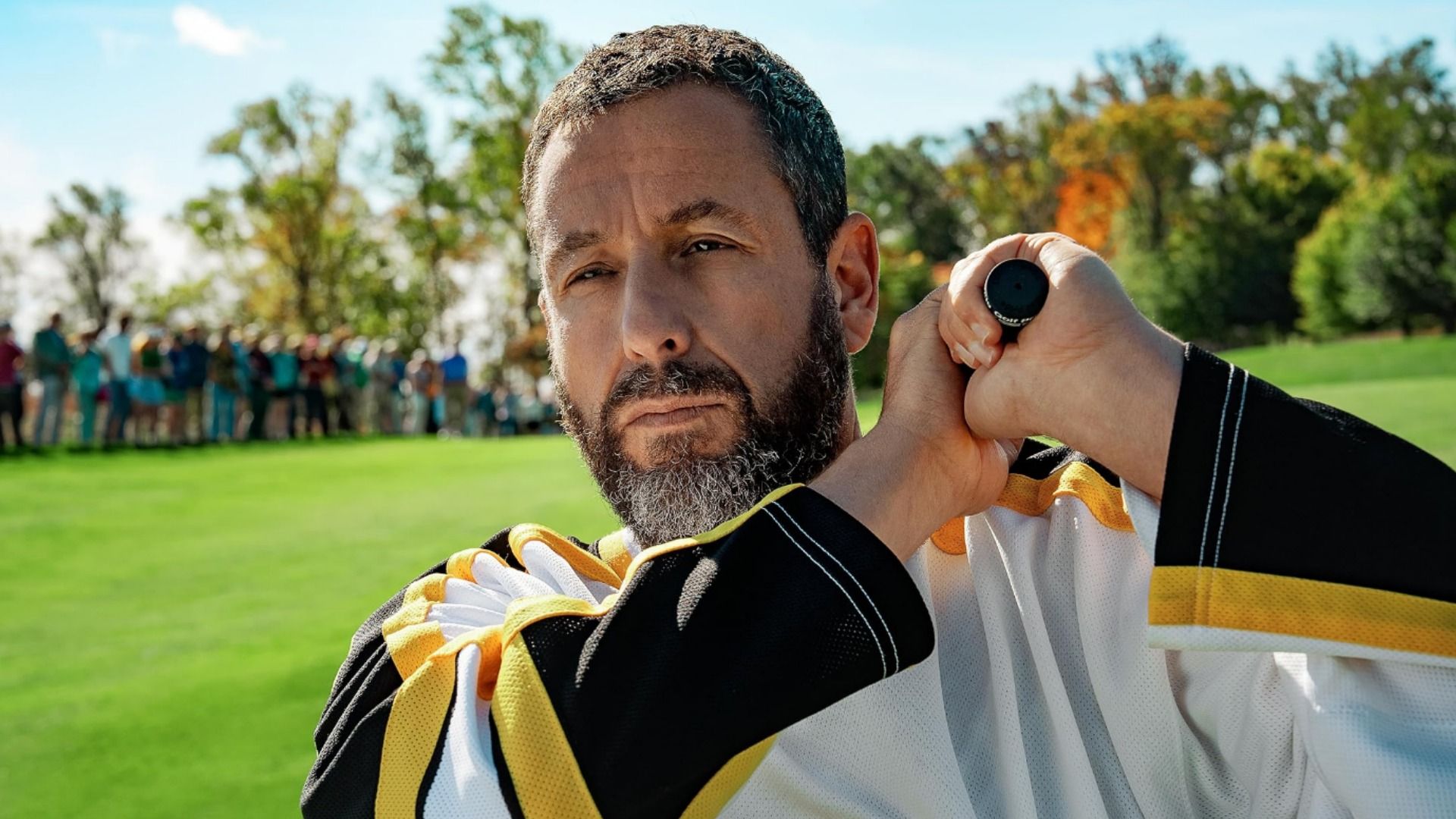 L'attore Adam Sandler che tiene una mazza da golf in piedi su un campo da golf