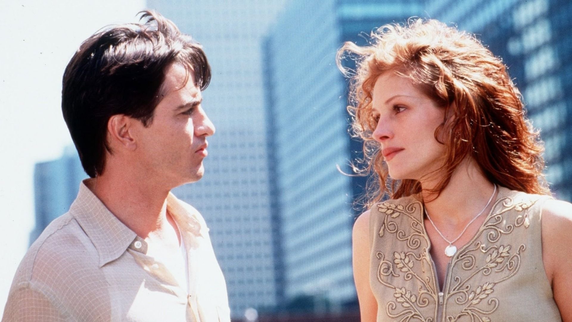 L'attore Dermot Mulroney in camicia chiara guarda l'attrice Julia Roberts sullo sfondo di grattacieli