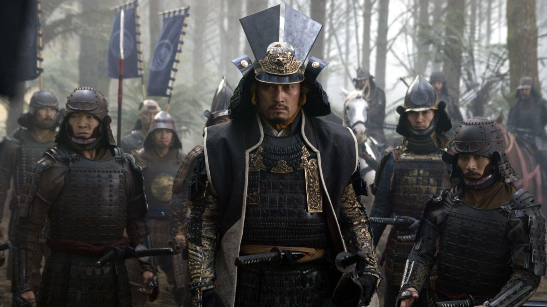 L'attore Ken Watanabe in armatura samurai scura sta in piedi circondato da altri samurai