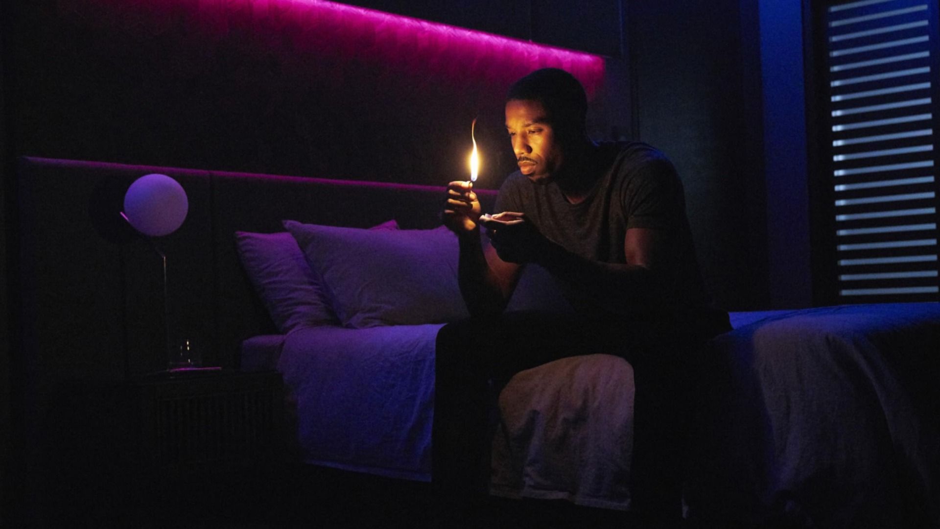 L'attore Michael B. Jordan seduto su un letto con un fiammifero in mano