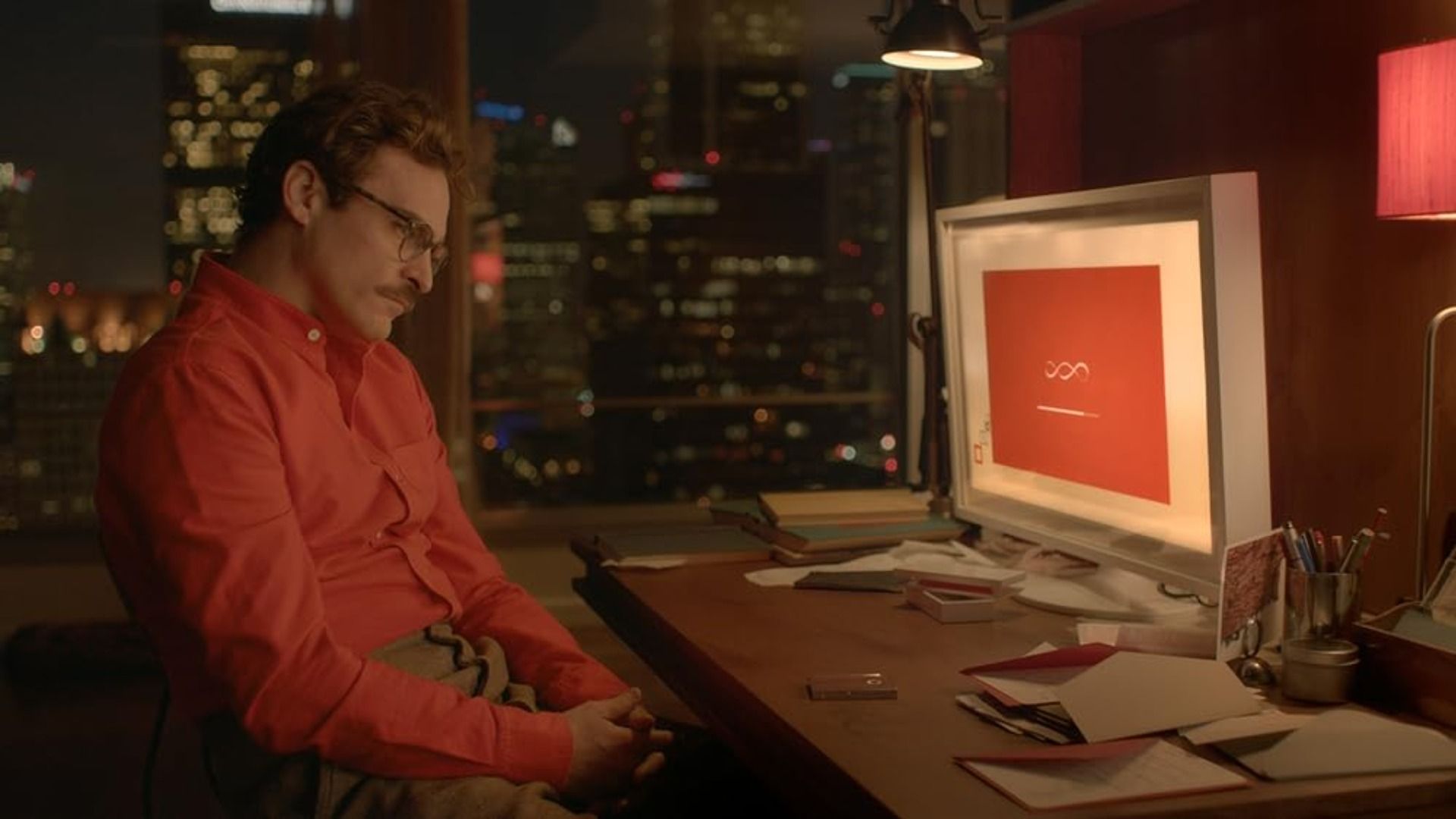 L'attore Joaquin Phoenix in una camicia rossa siede a un tavolo con un computer sopra