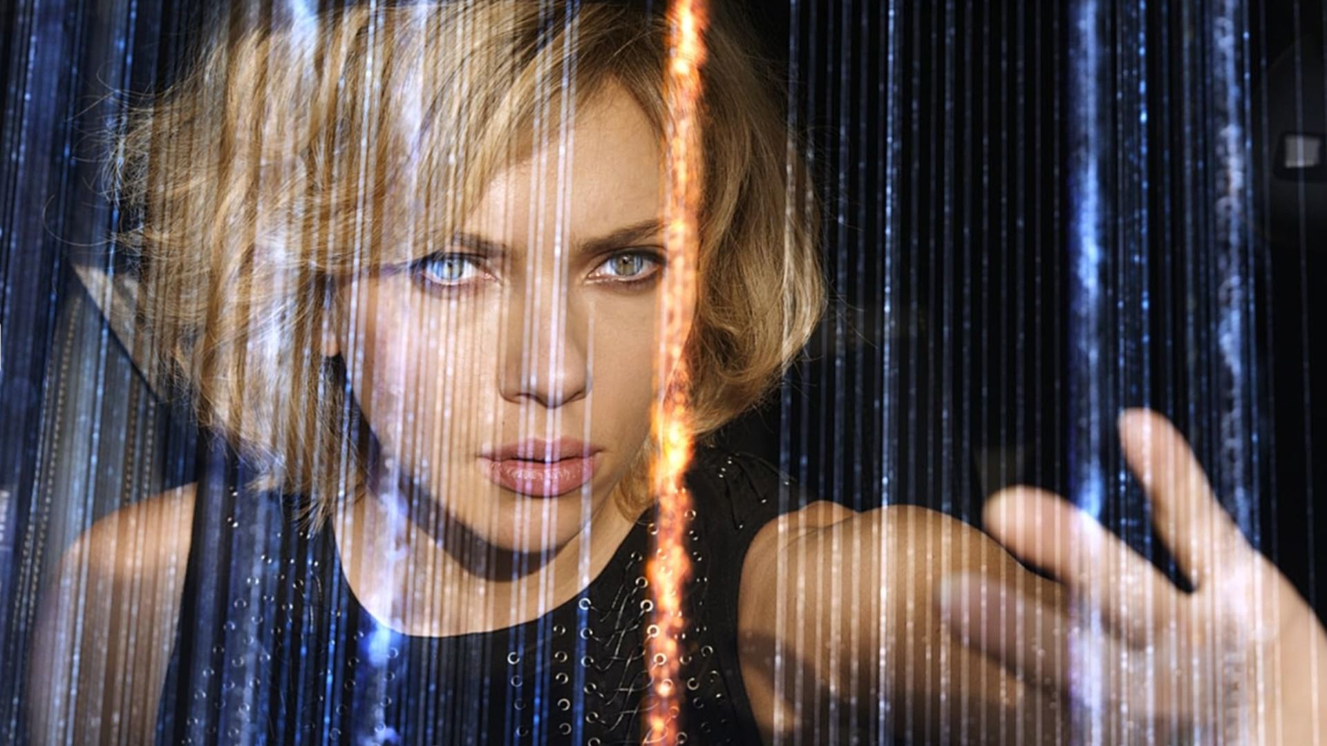 L'attrice Scarlett Johansson in un vestito nero con la mano alzata tra linee scintillanti