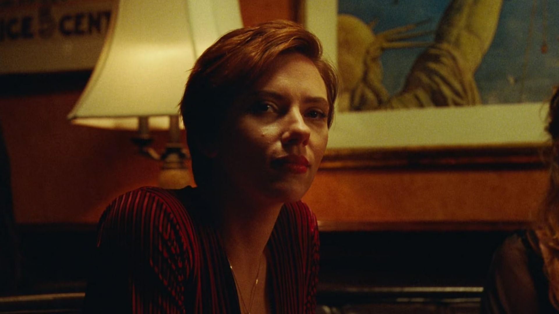 L'attrice Scarlett Johansson in una camicetta rossa siede accanto a una lampada