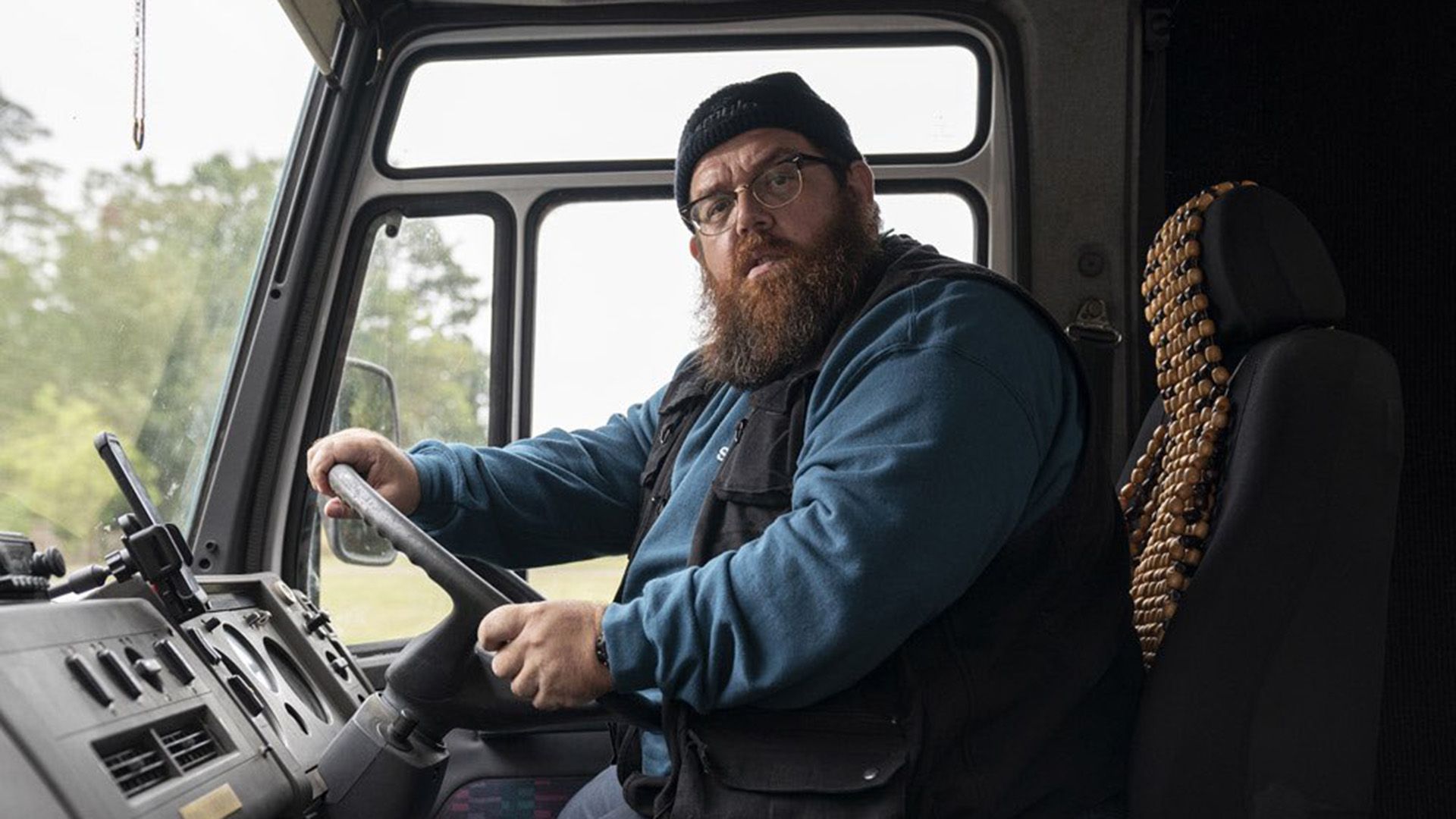 Nick Frost con occhiali e cappello seduto al volante di un camion, guarda verso la telecamera