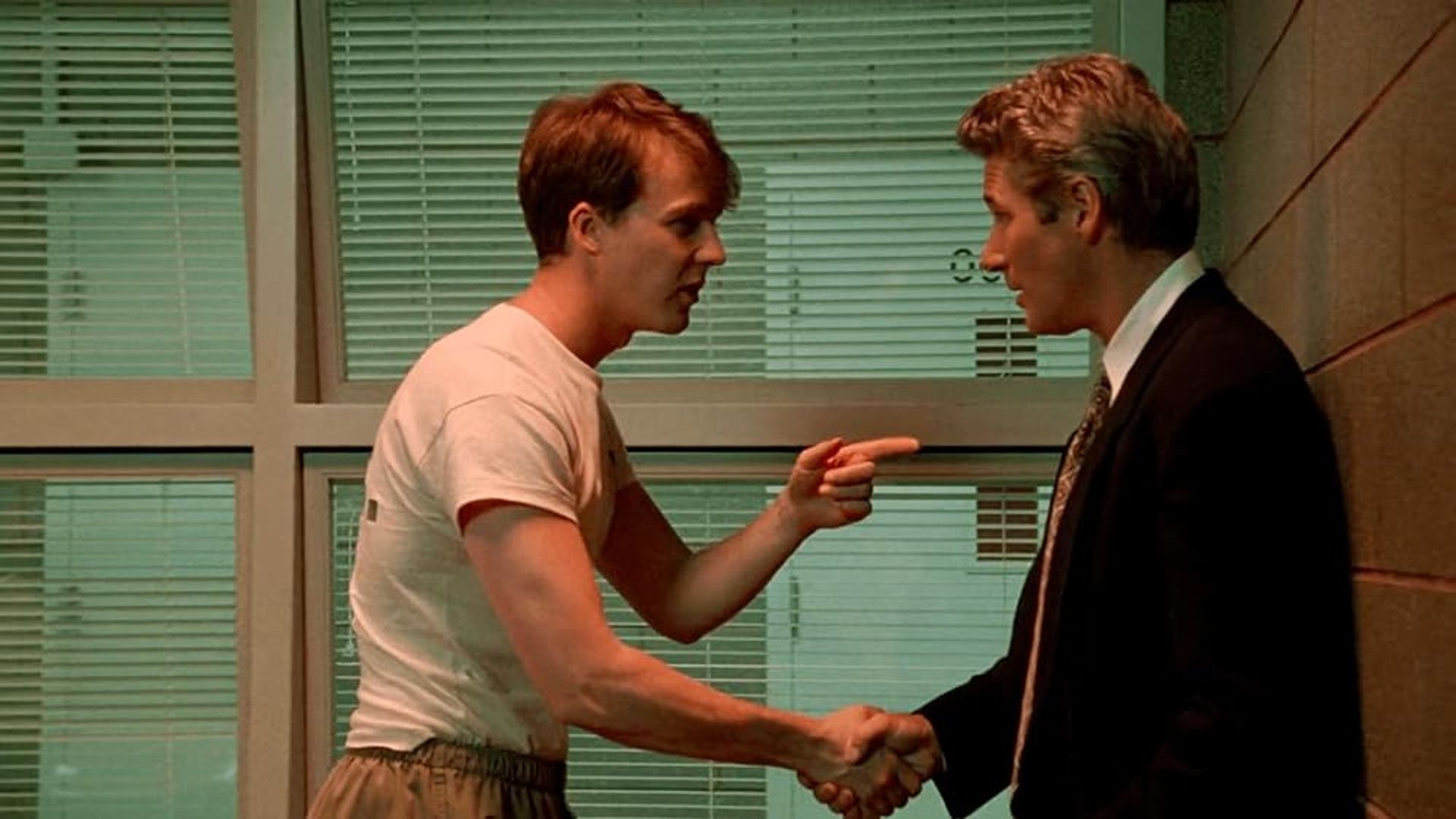 Edward Norton in maglietta stringe la mano a Richard Gere in giacca e cravatta, che lo indica con il dito