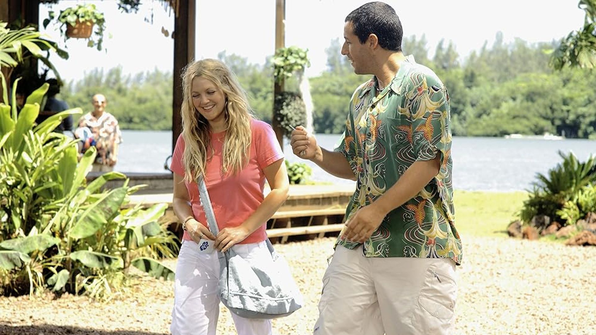 Drew Barrymore e Adam Sandler che parlano su una spiaggia soleggiata con vegetazione e acqua sullo sfondo