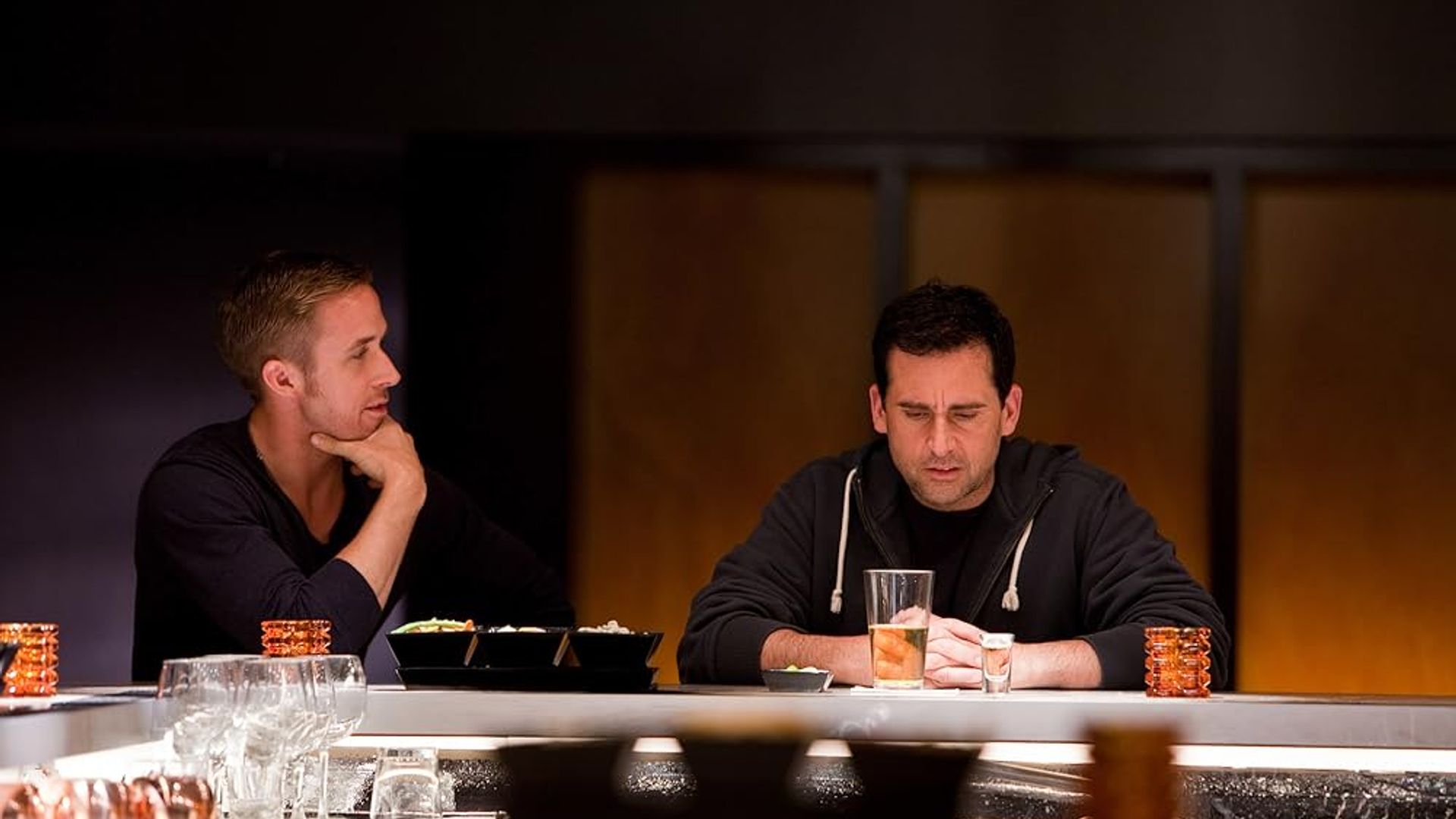 Ryan Gosling e Steve Carell seduti al bancone di un bar, uno fissa pensieroso il suo bicchiere, l'altro osserva